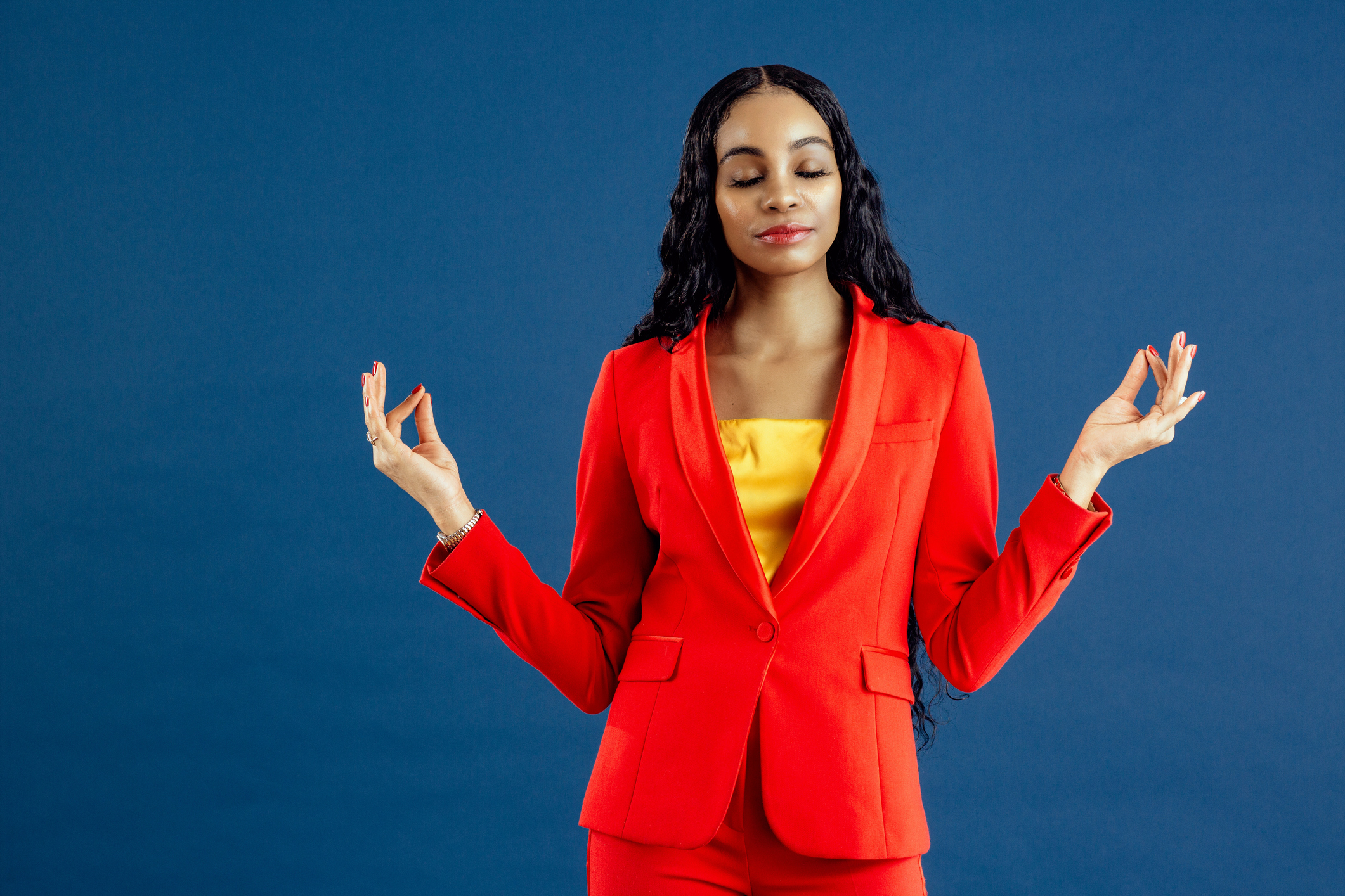 Portrait of a  young woman in red business suit with hands out and fingers together, meditating and focusing