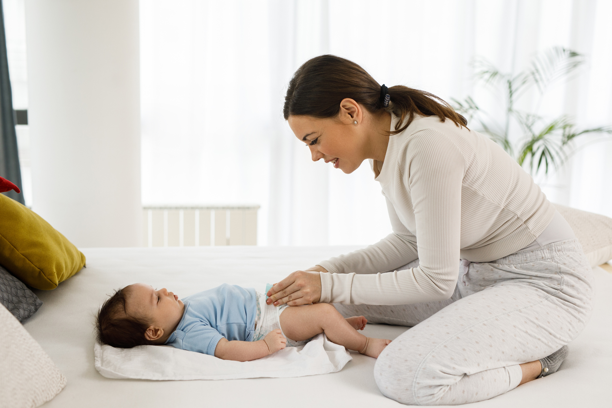 Young mother with her little baby boy at home changing diapers