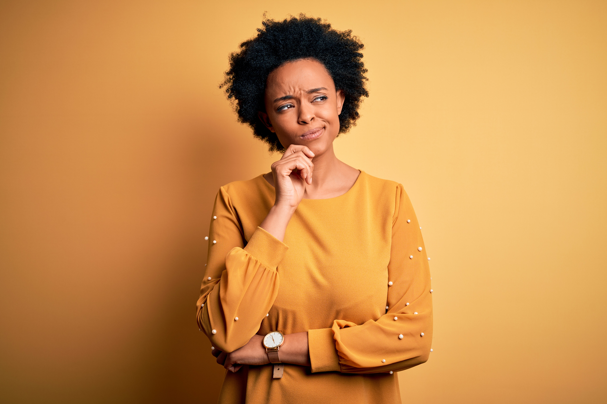 Young beautiful African American afro woman with curly hair wearing casual t-shirt with hand on chin thinking about question, pensive expression. Smiling with thoughtful face. Doubt concept.