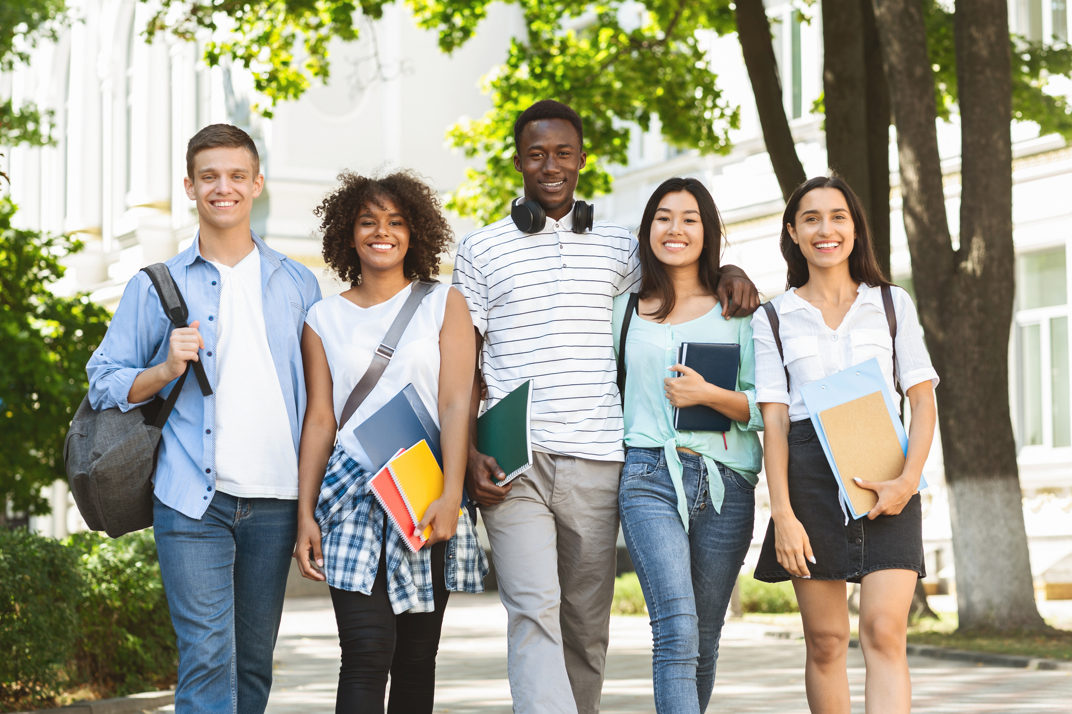 Cheerful college students walking out of campus together, posing outdoors