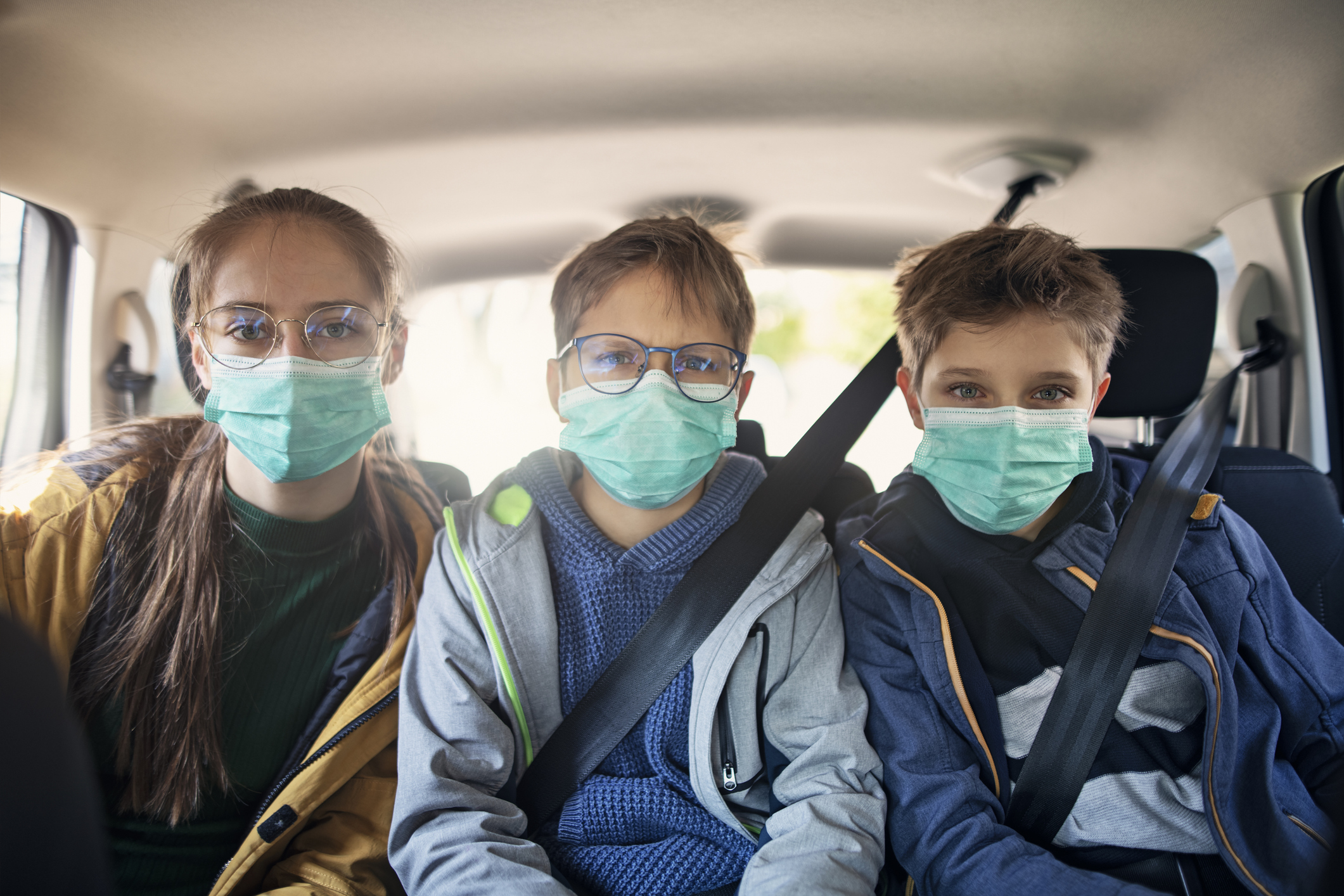 Three kids wearing anti virus marks travelling by car