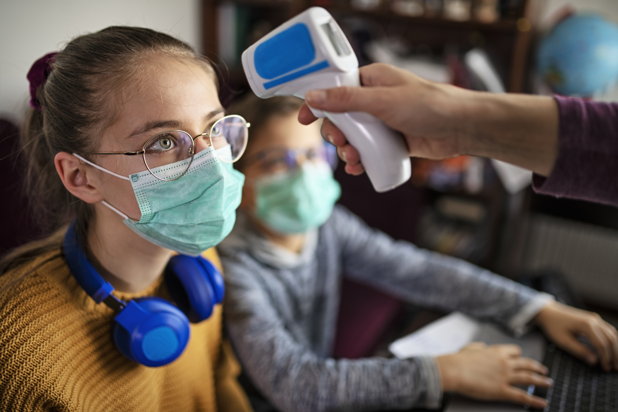 Mother taking temperature of kids attending to online school class.