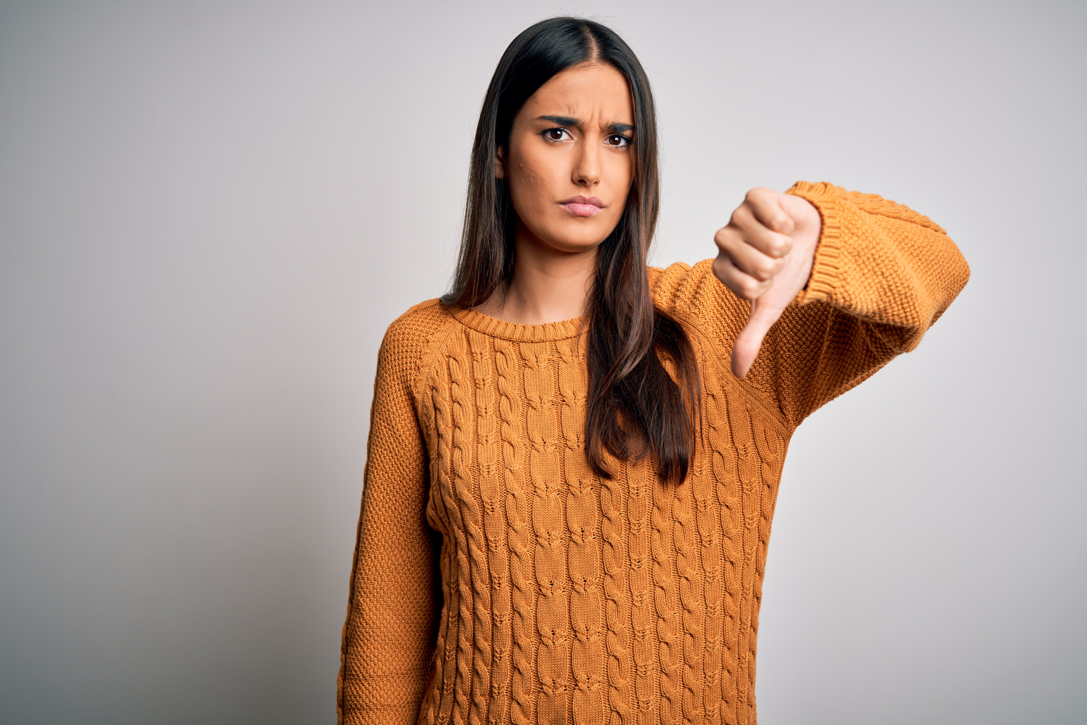 Young beautiful brunette woman wearing casual sweater over isolated white background looking unhappy and angry showing rejection and negative with thumbs down gesture. Bad expression.