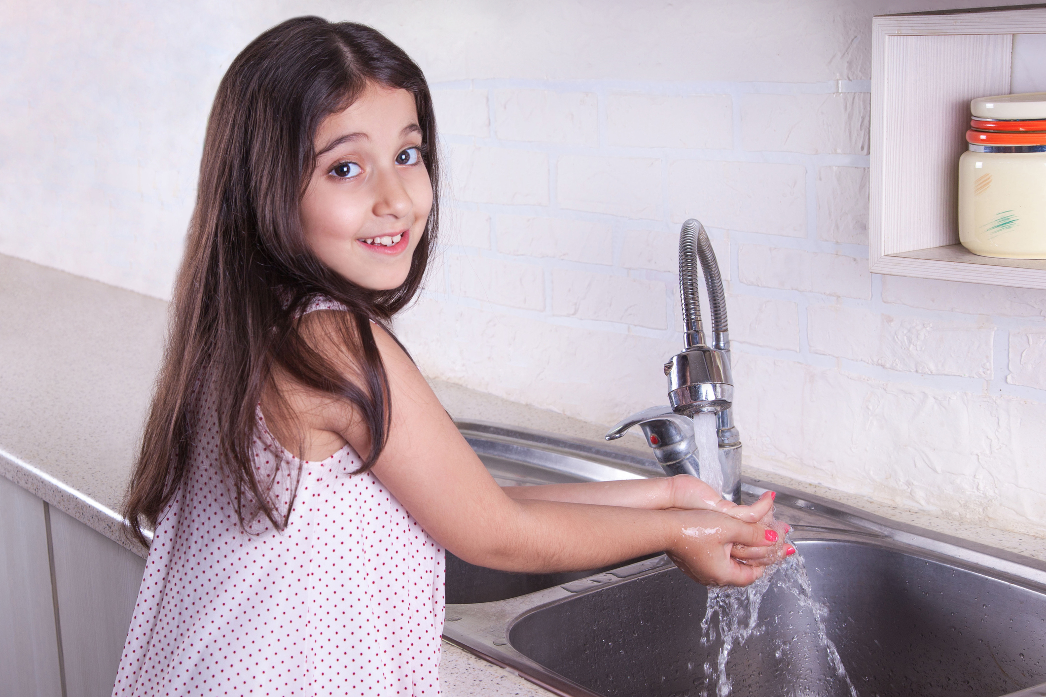 Washing hands. Beautiful happy girl washing her hands and looking at camera with toothy smile and happiness.