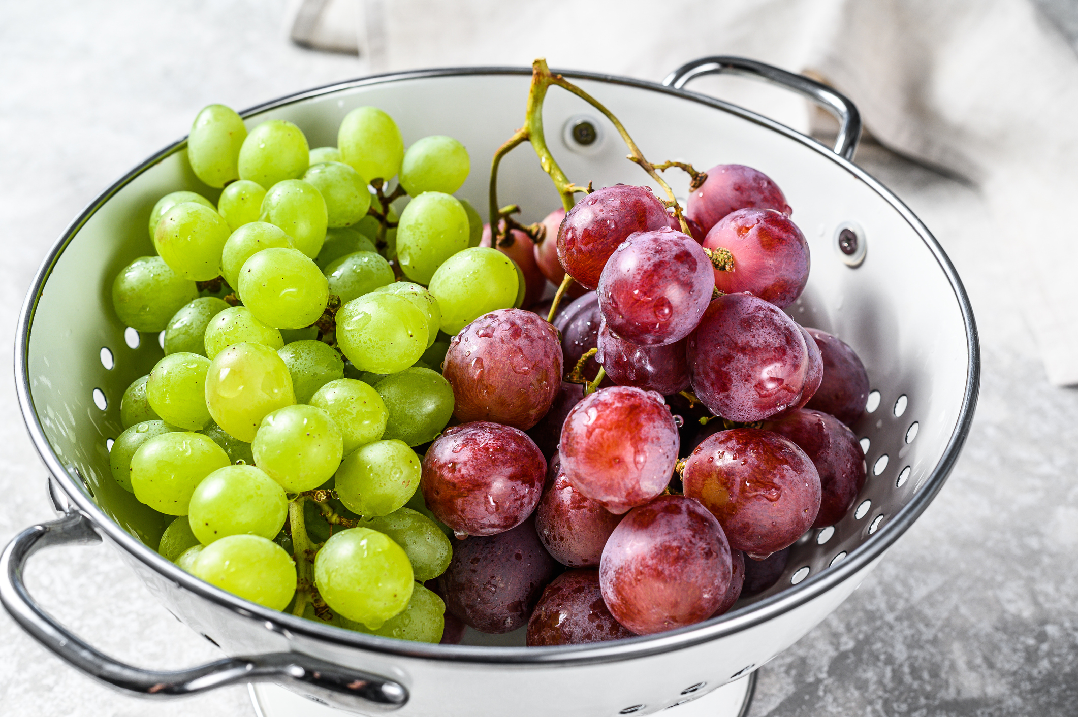 Two varieties of grapes, red and green in a colander. Gray background. Top view