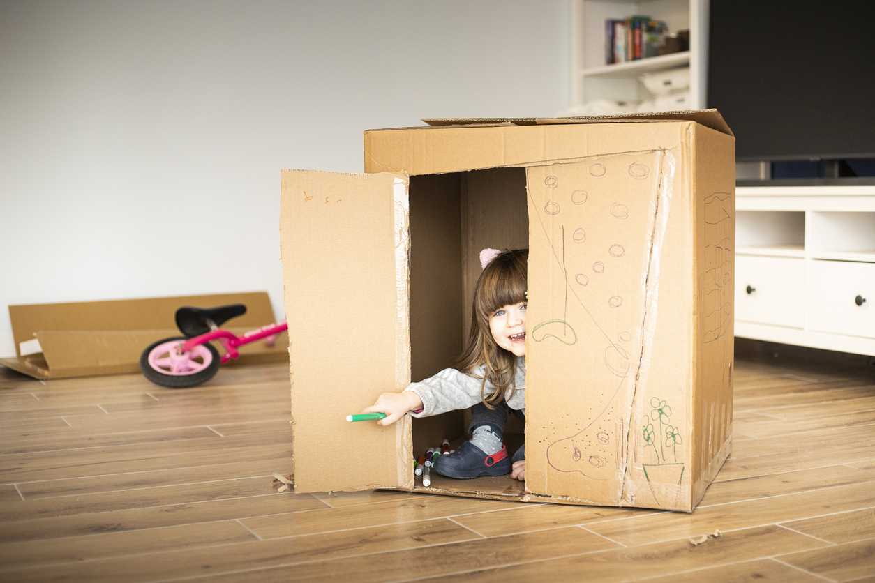 child girl looking out of a cardboard playhouse