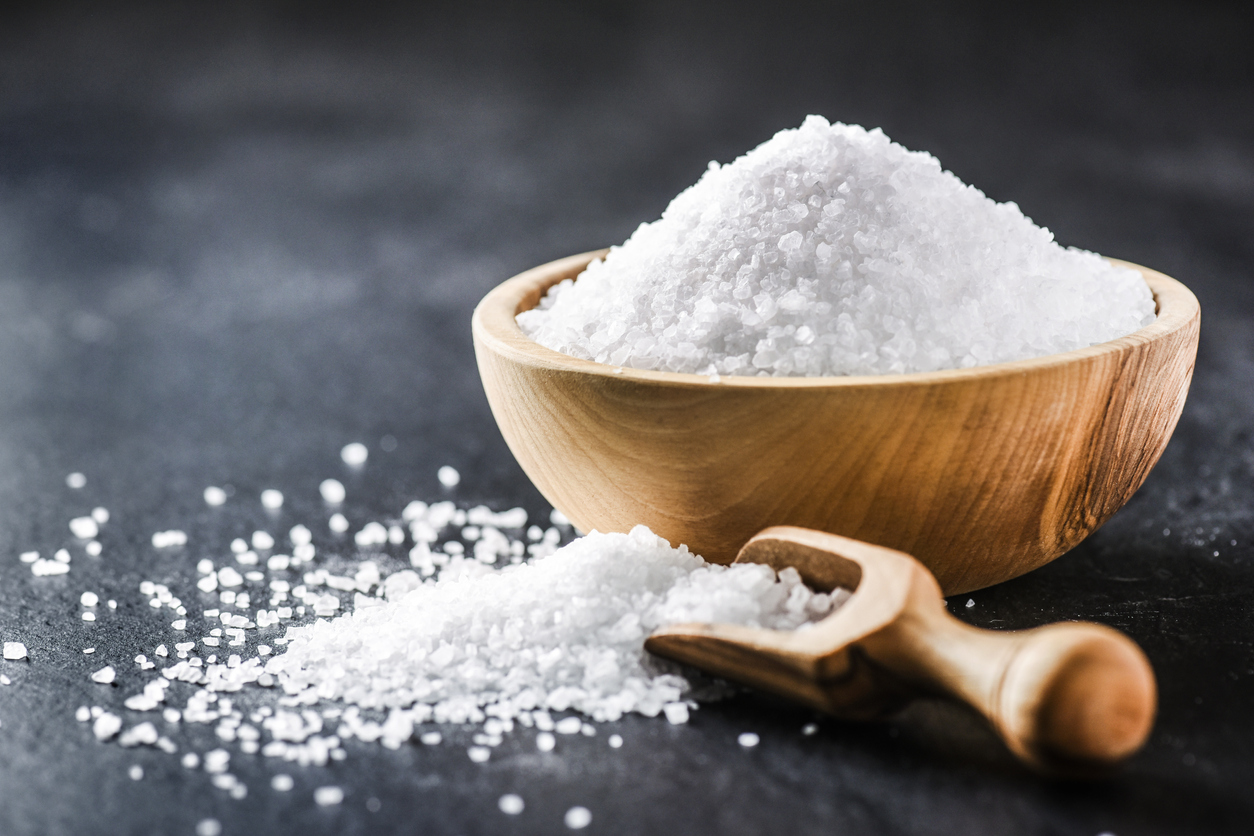 Salt. Glass salt shaker on dark stone table.  A pile of salt top view and wooden bowl