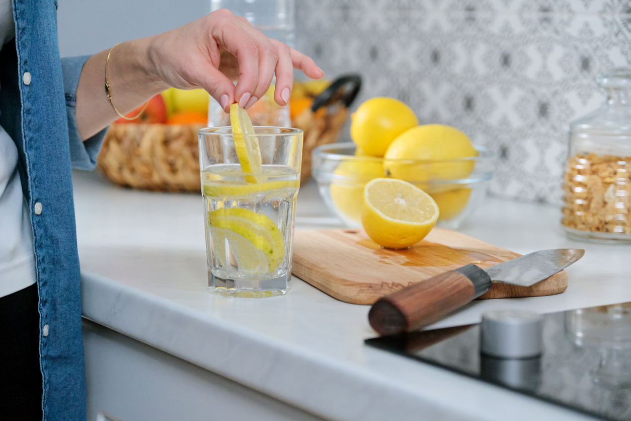 Female hand with slice of lemon in kitchen, with sparkling water with lemon