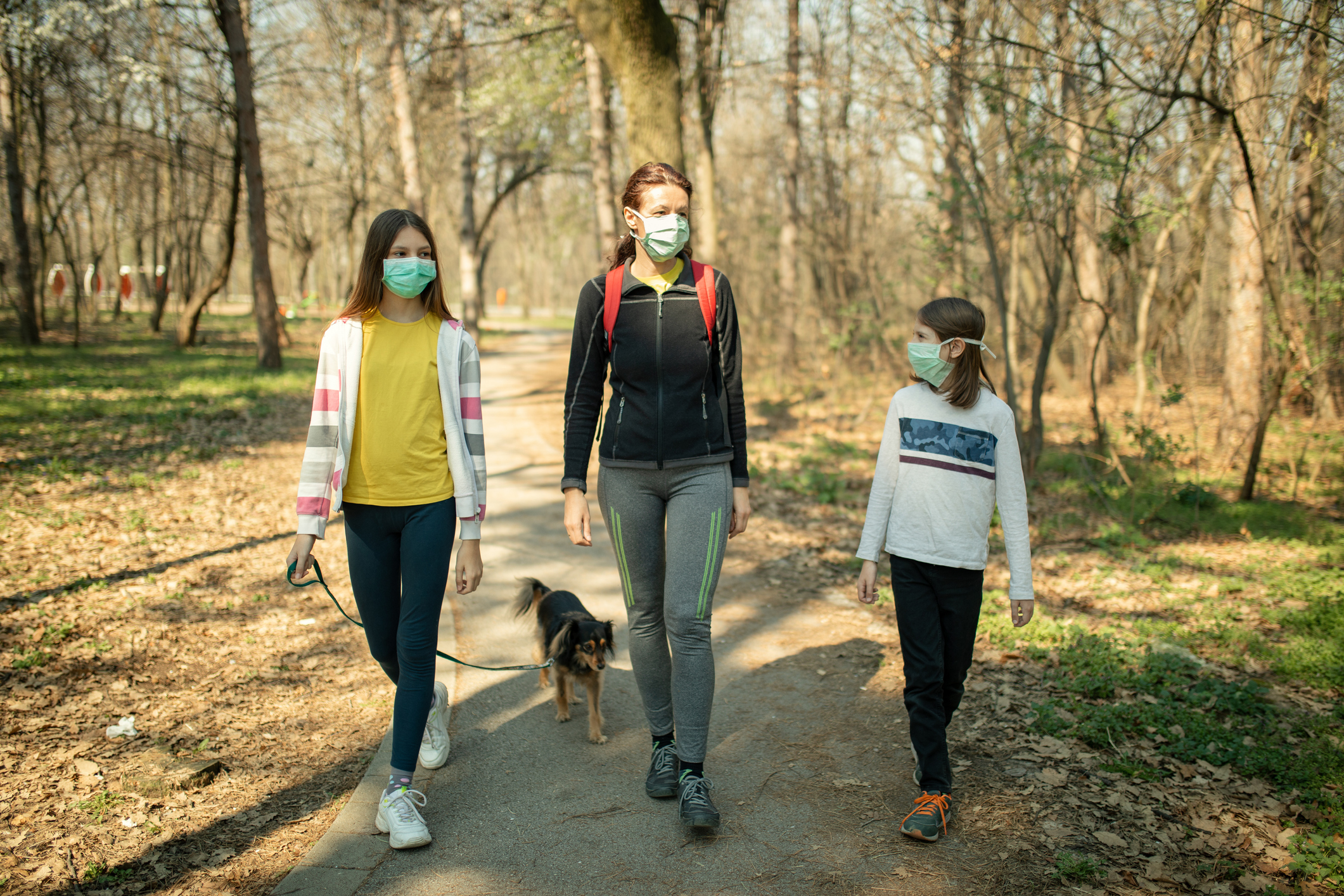 Family walking with their dog in park and wearing mask