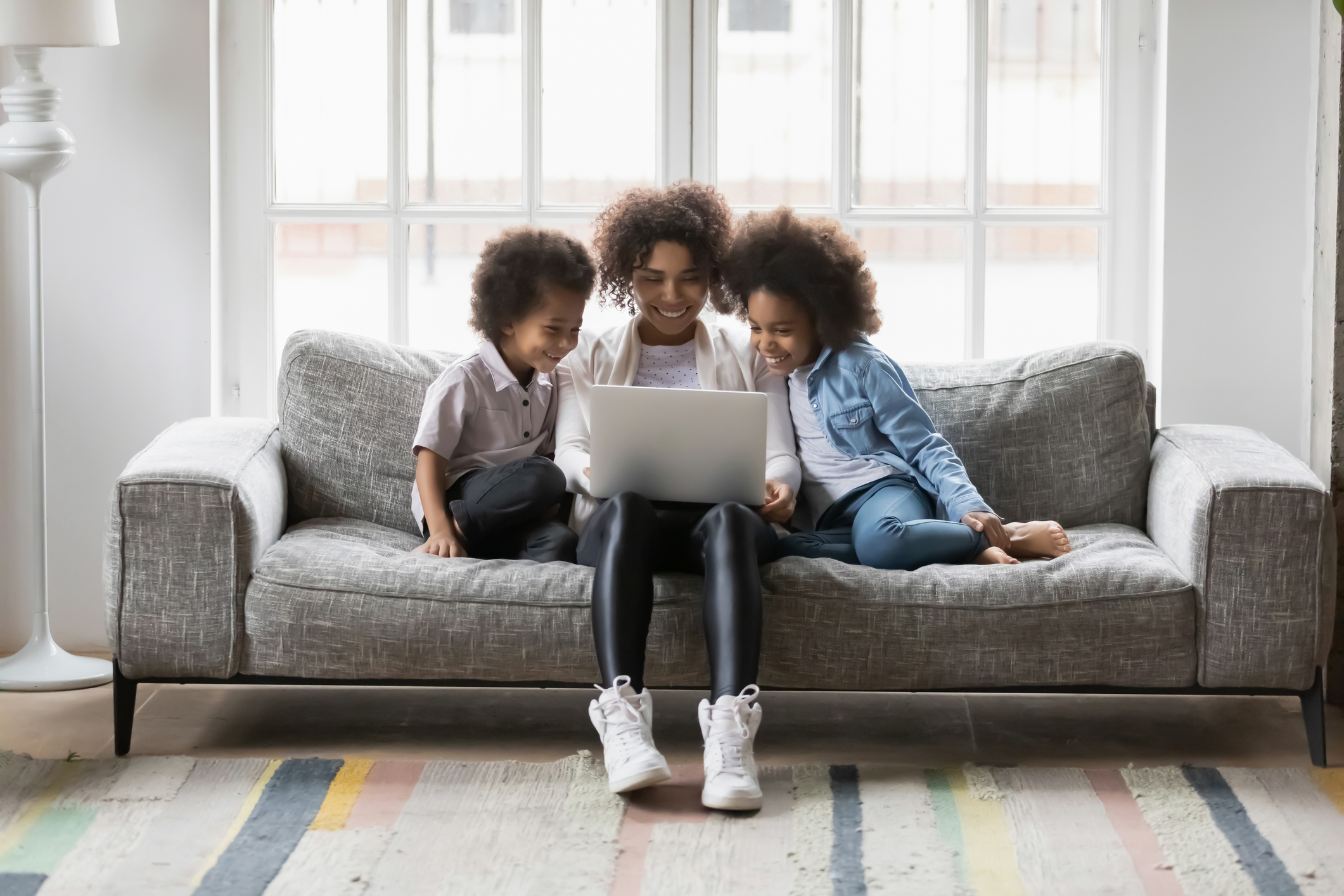 African mother and little children sitting on couch using laptop