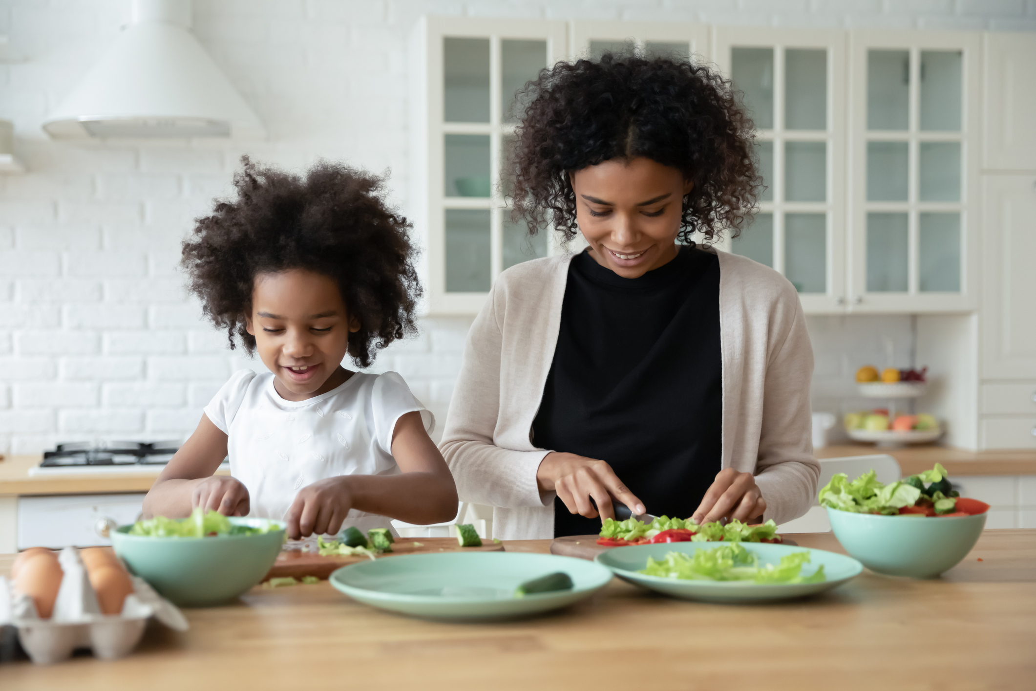 Multiethnic young mom and little daughter cooking at home together