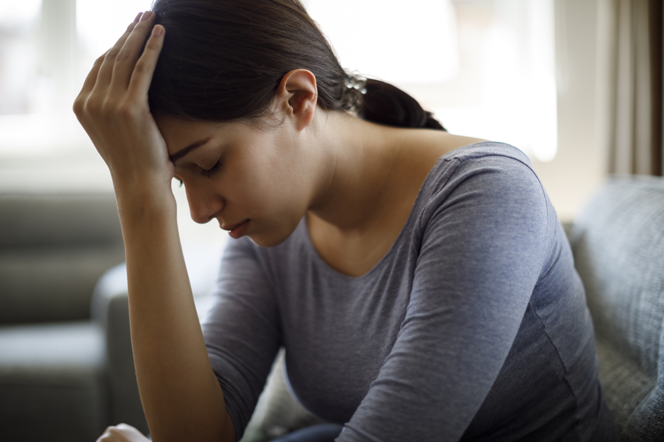 Upset woman sitting on sofa alone at home