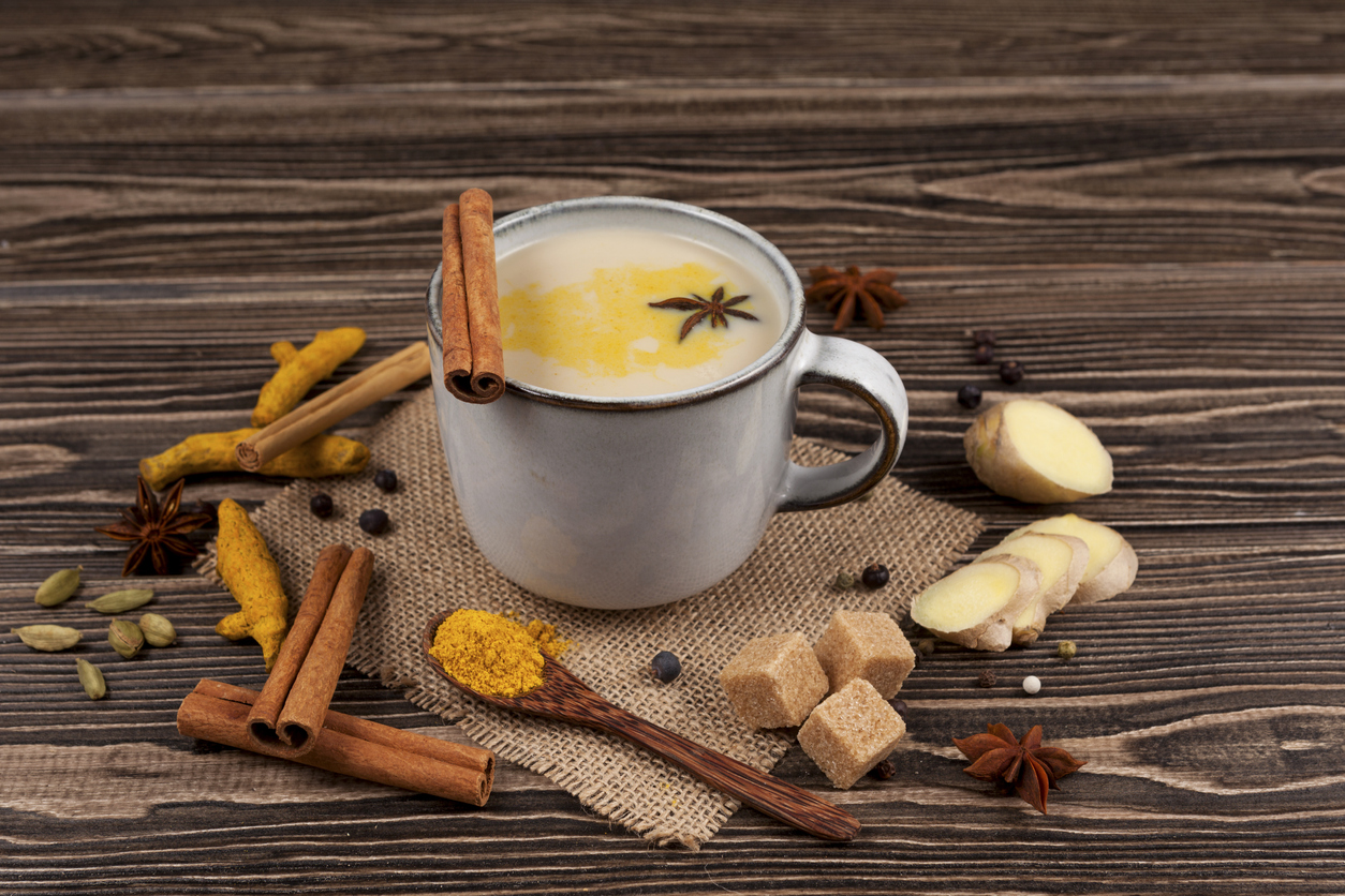 A popular Indian drink  Masala tea or Masala chai. Prepared with the addition of milk, variety of spices and spices. A cup on a wooden table next to the ingredients. Rustic style. Closeup