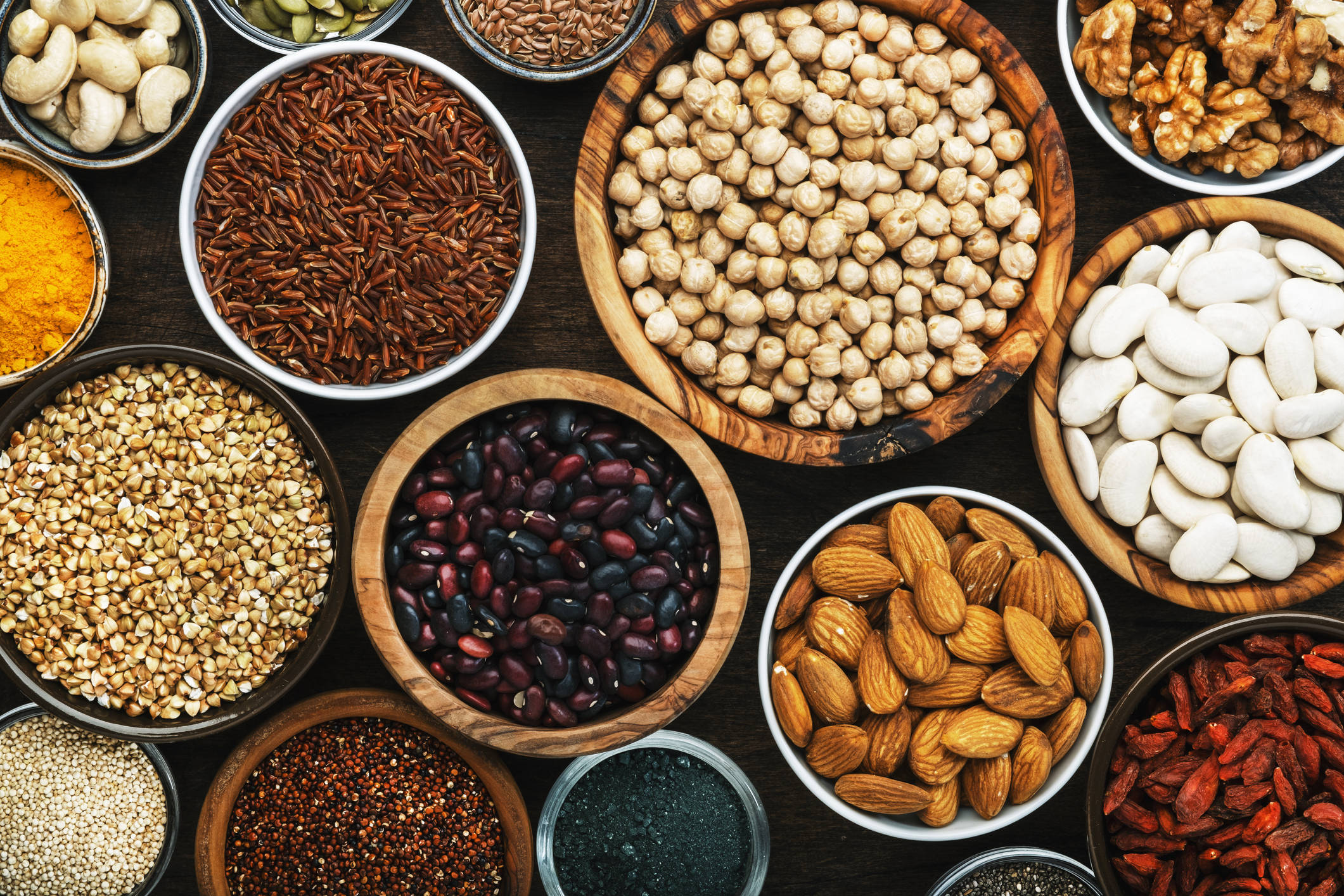 Superfoods, legumes, nuts, seeds and cereals set in bowls on wooden background. Superfood as chia, spirulina, beans, goji berries, quinoa, turmeric, mung bean, buckwheat, lentils, flax seed, wild rice and almond. Copy space, top view