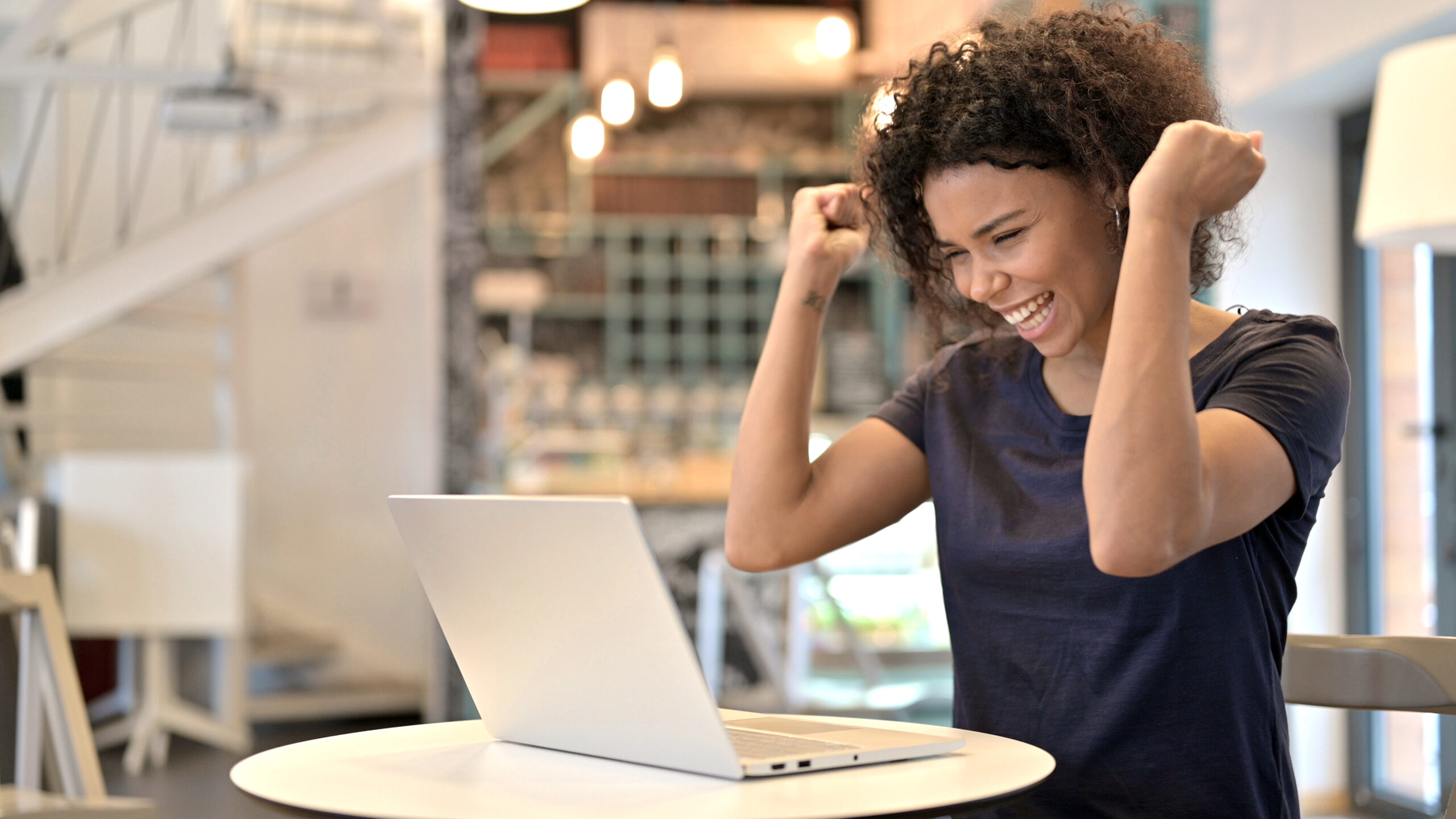 Young African Woman Celebrating Success on Laptop in Cafe