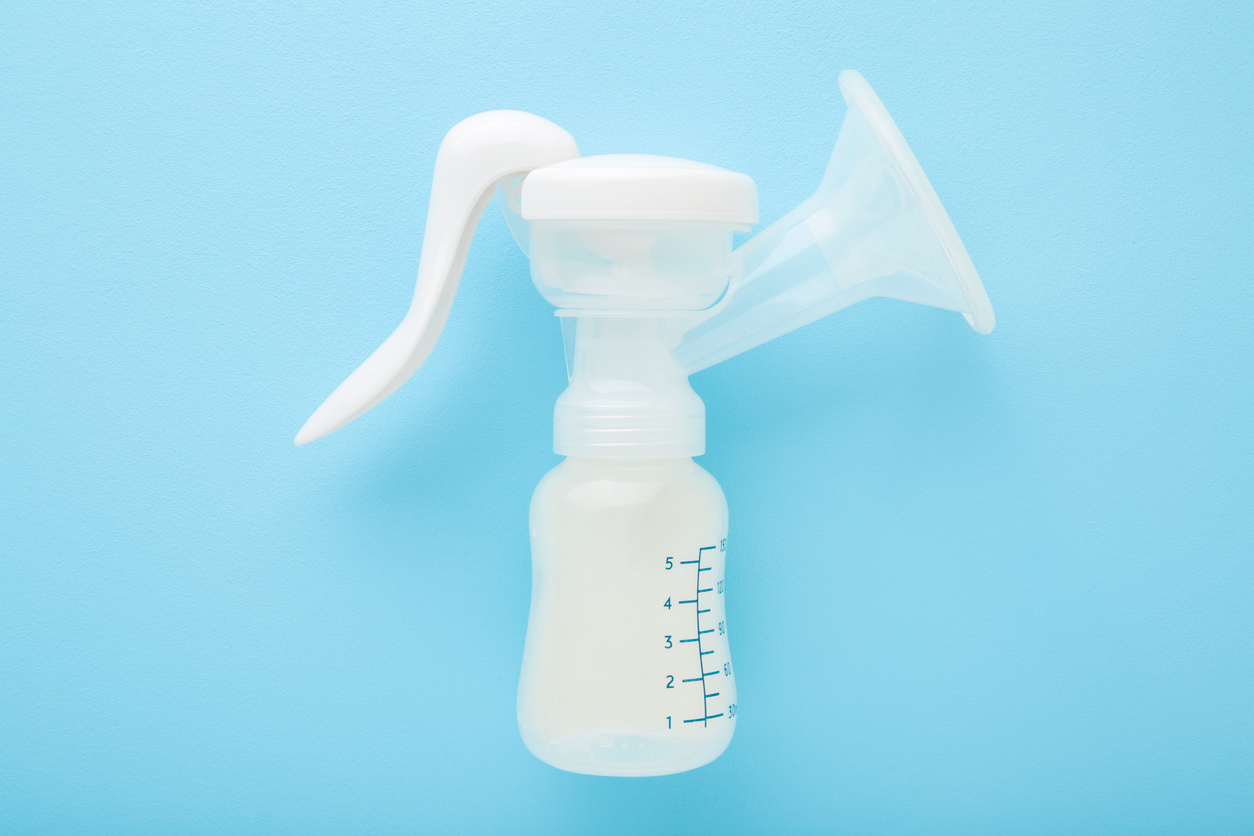 Plastic breast pump bottle on light blue table background. Pastel color. Closeup. Preparing milk for baby feeding. Top down view.