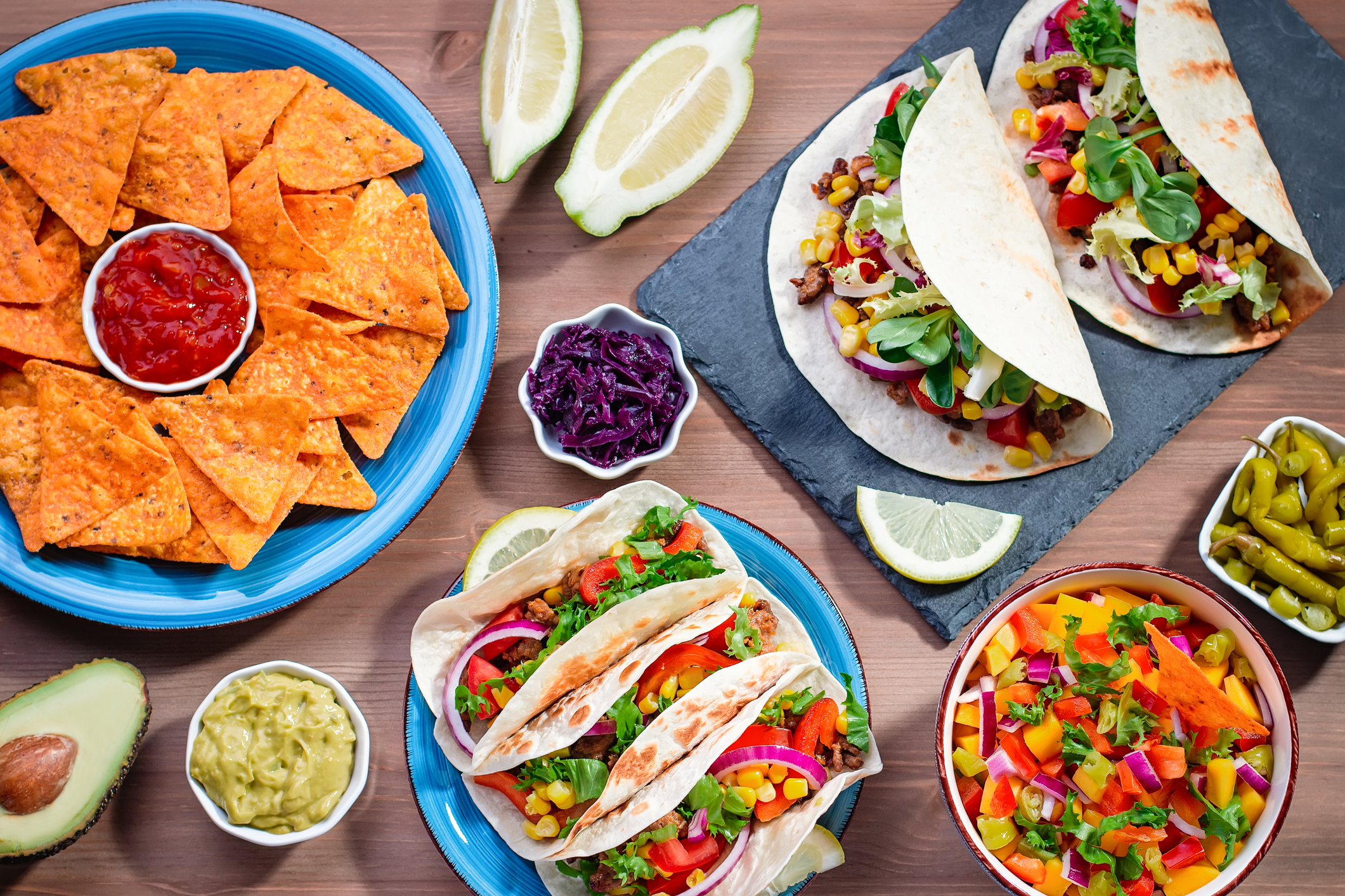 Table with tacos, mango salsa, nachos with sauce, guacamole, lemon beer. Appetizers and traditional mexican dishes for cinco de mayo or taco tuesday on wooden table top, copy space