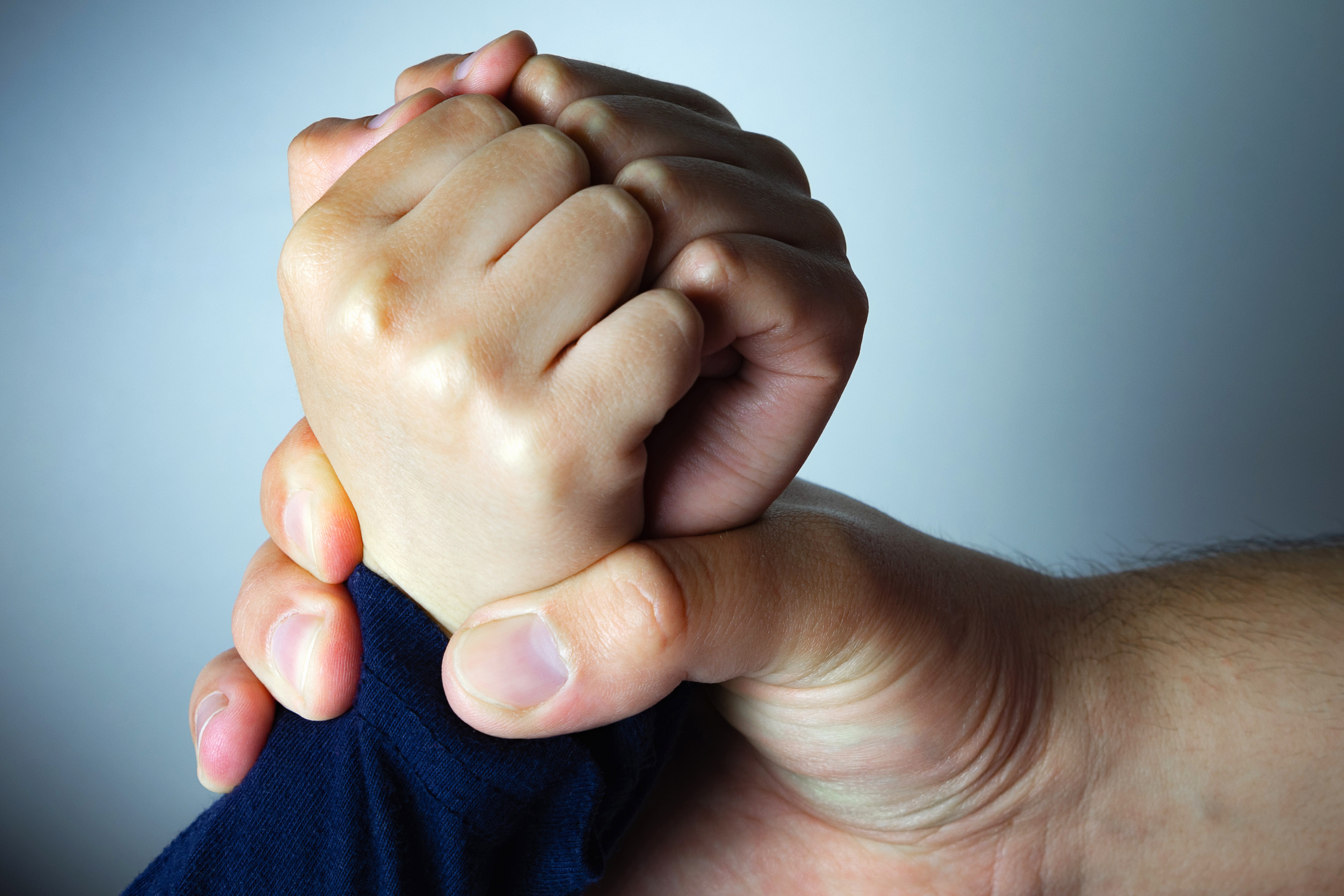 Father roughly holds the hands of his son. Child abuse, domestic violence.