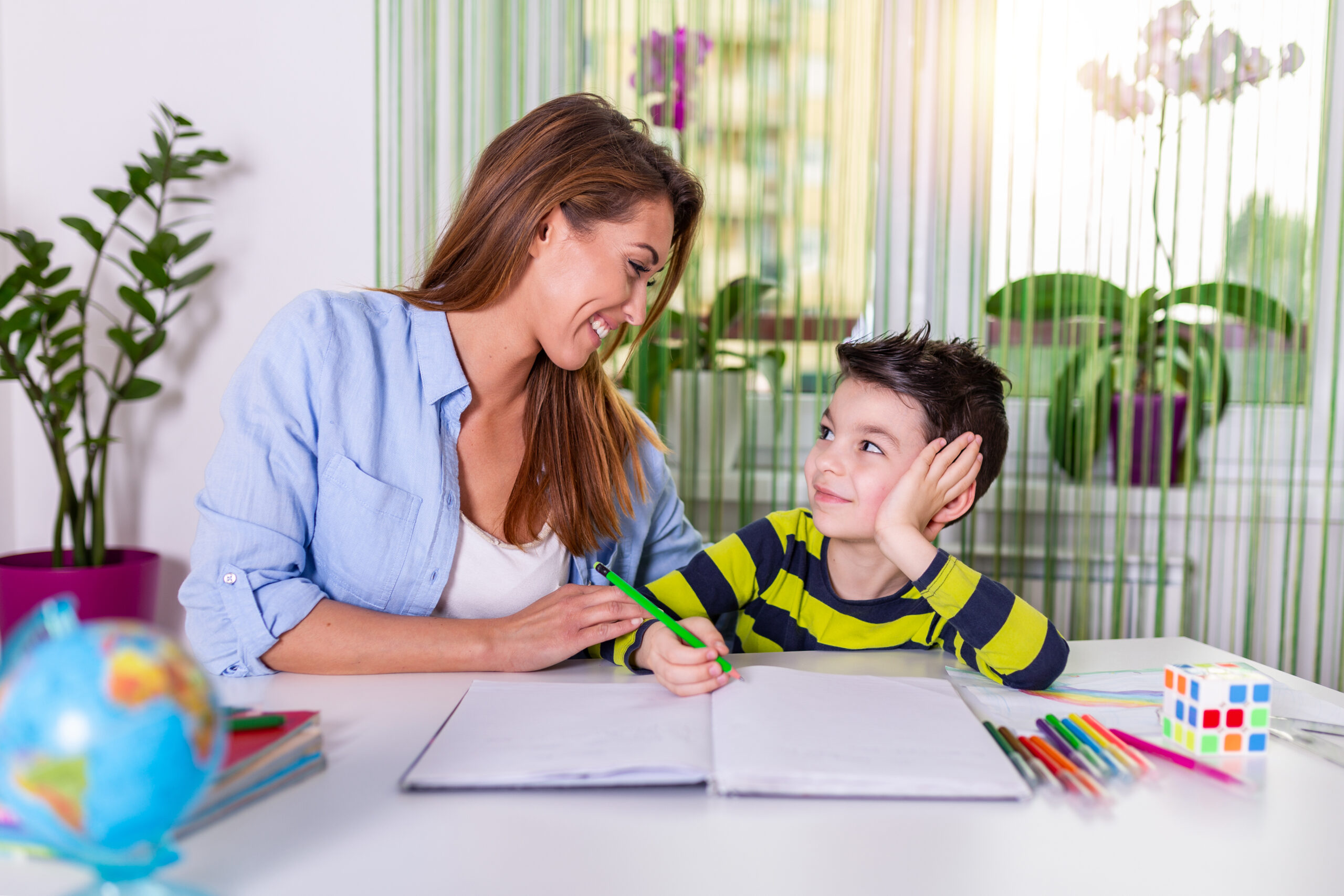 Cute boy with mother doing homework at home. A mother helps her little son to do her homework for the school. Education and family concept