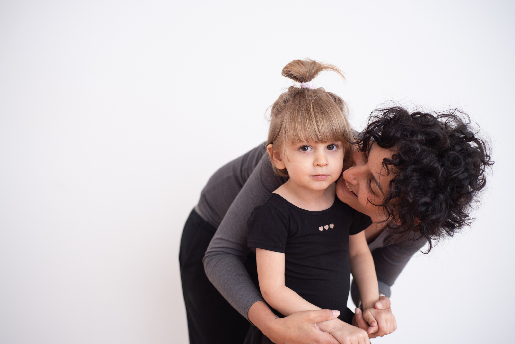 Portrait of Proud Mother Embracing her Little Daughter Dressed in Ballerina Dress Against White Background - stock photo