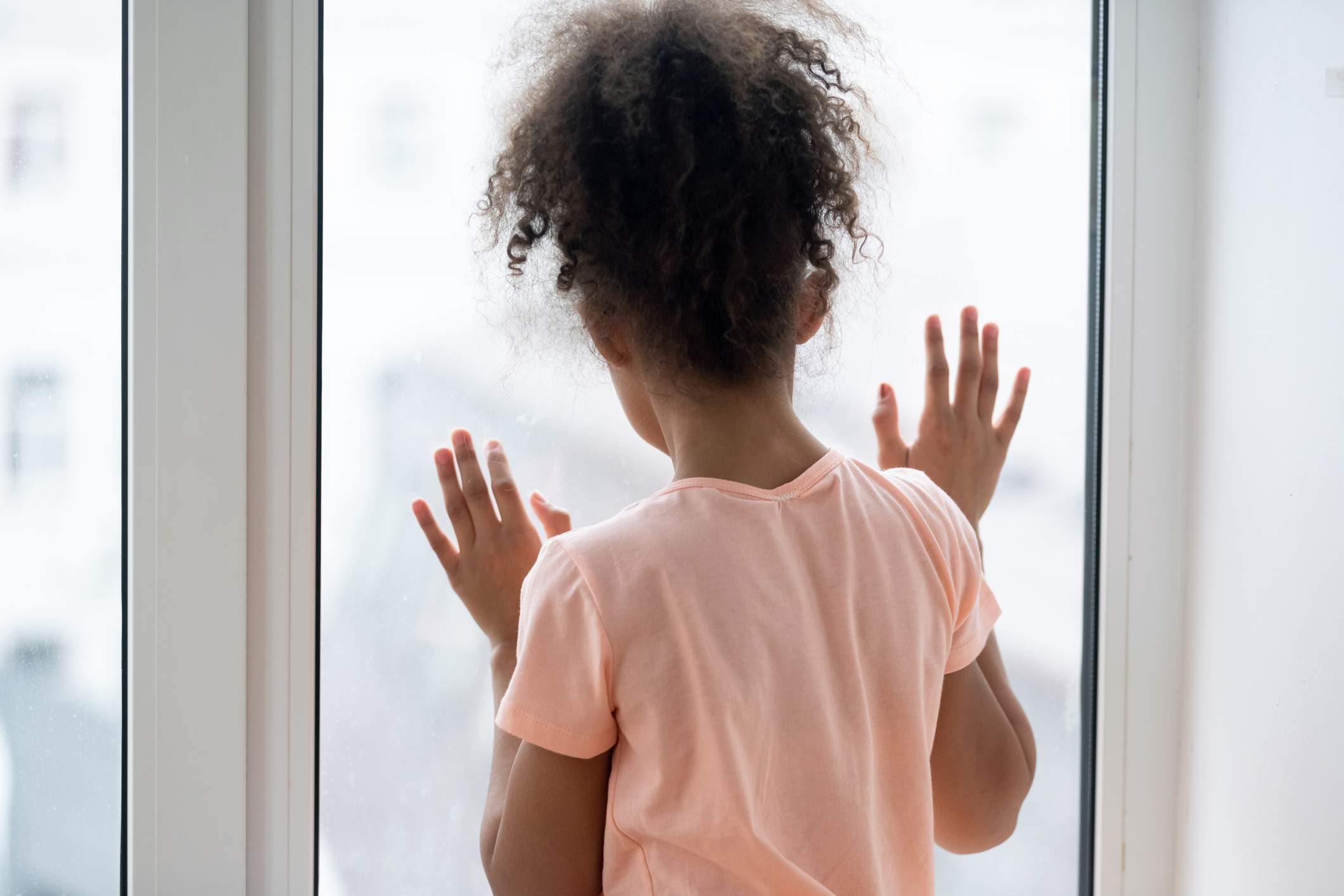 Rear view lonely African girl standing near window looking outside