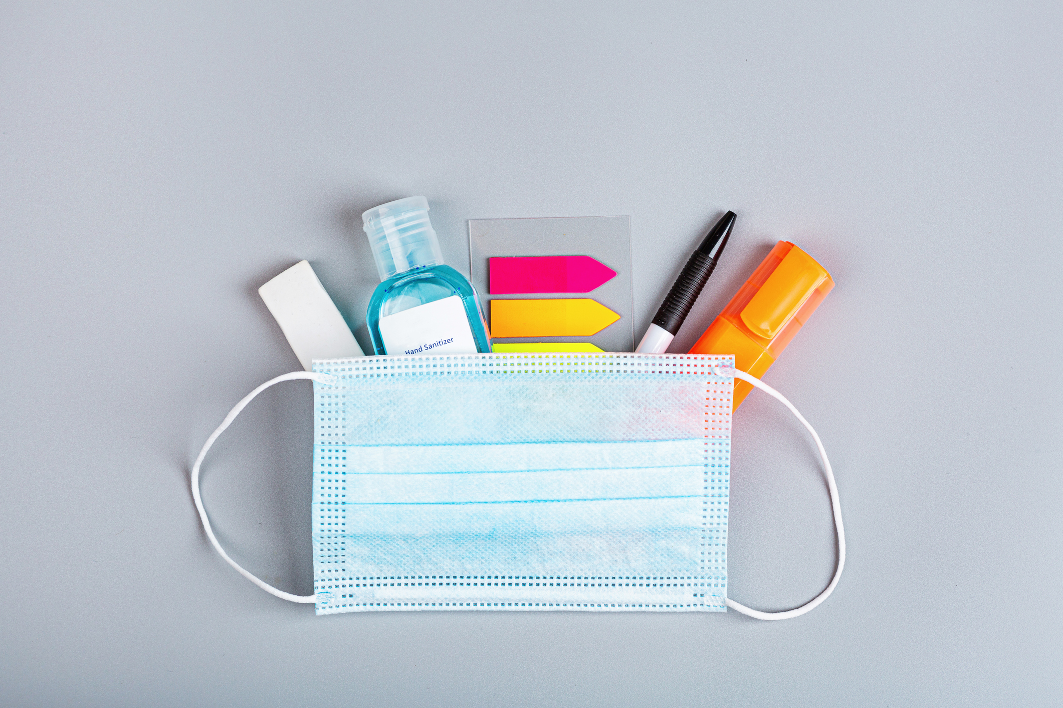 school supplies with medical face mask on a gray background. Protection of schoolchildren and students from the coronavirus covid-19, schooling in a pandemic. Flat lay, top view, mockup, template