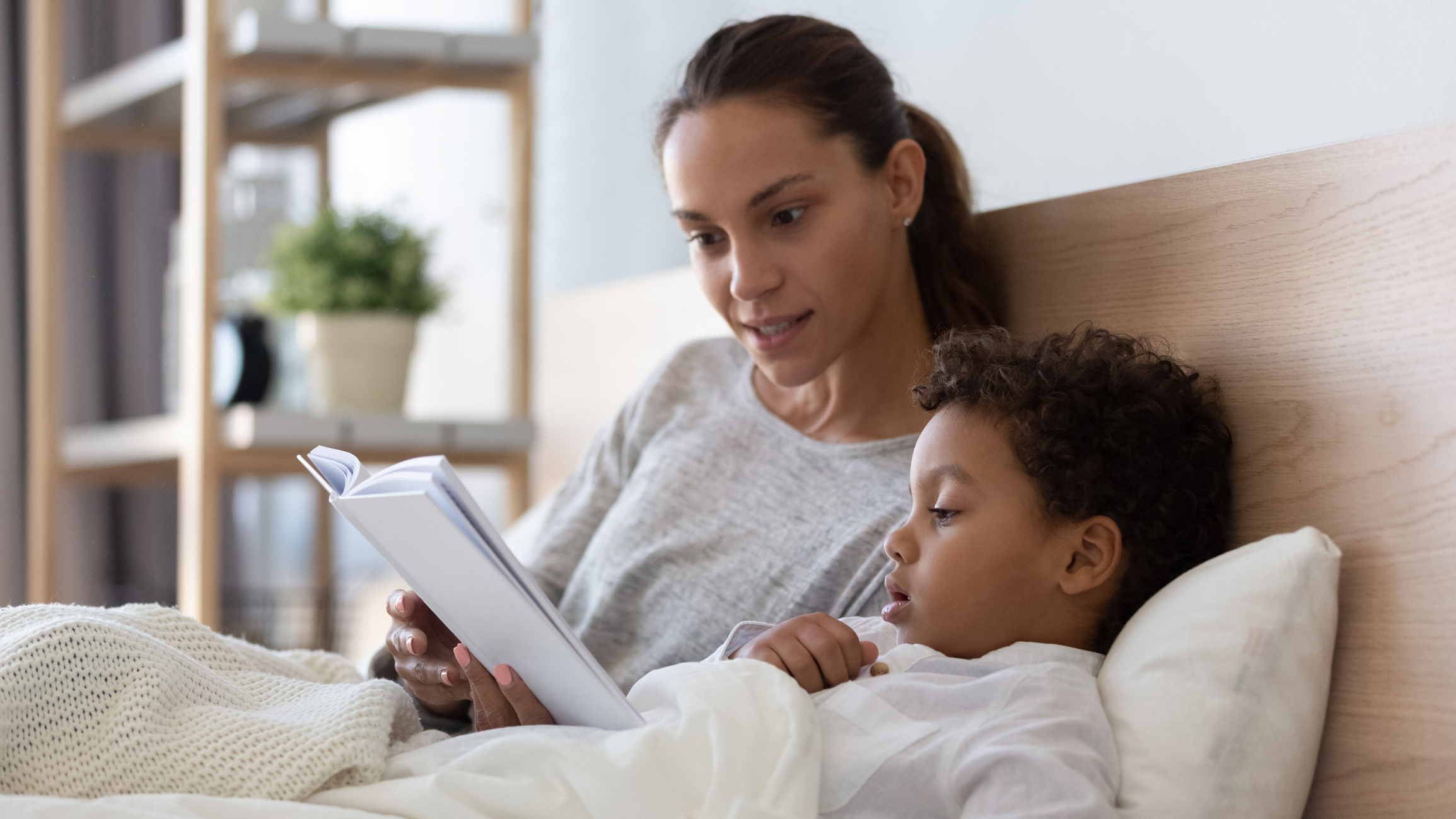 Caring mom reading book to little son in bed