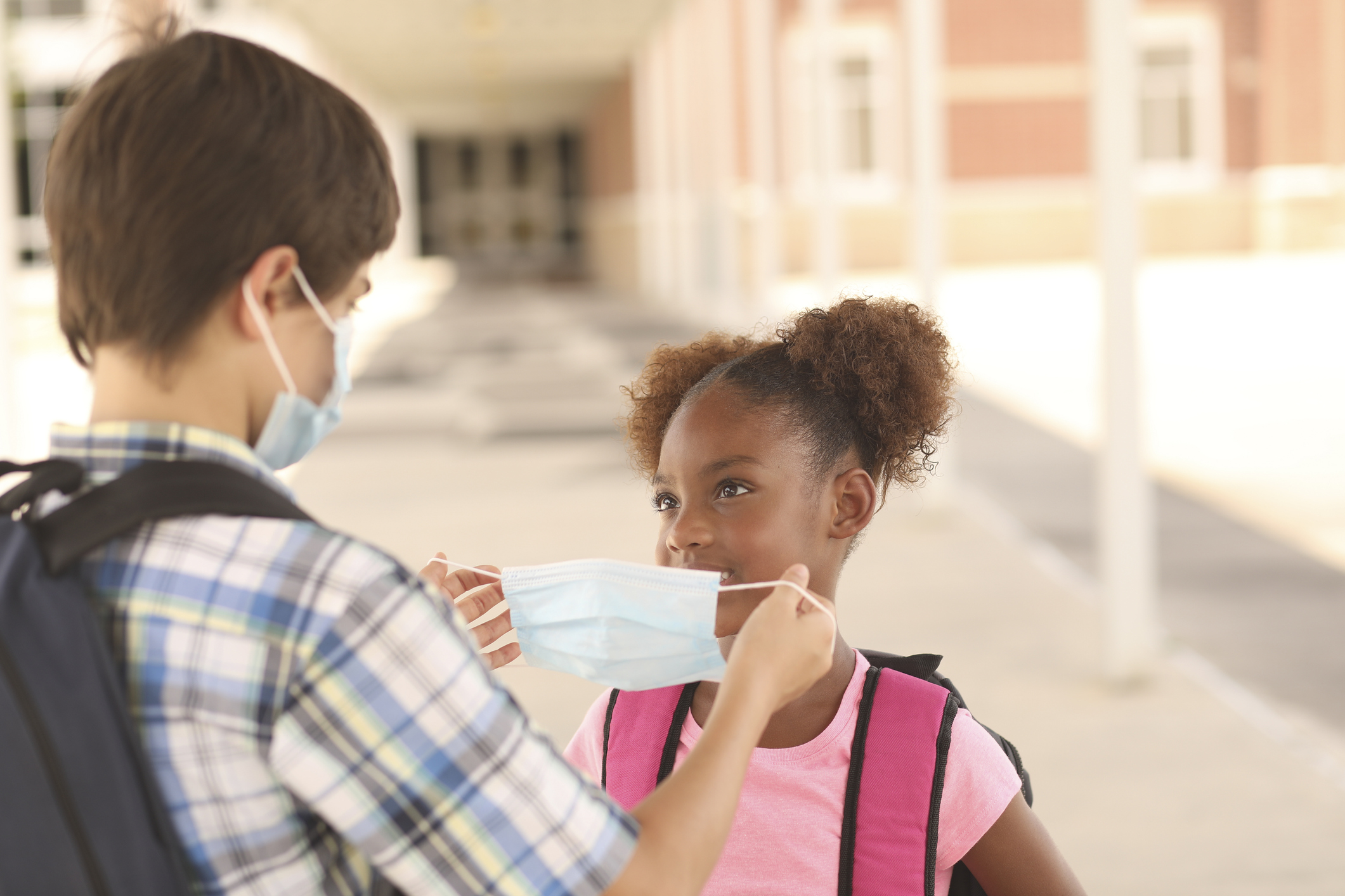 Friend helps younger student put on protective face mask. COVID-19.