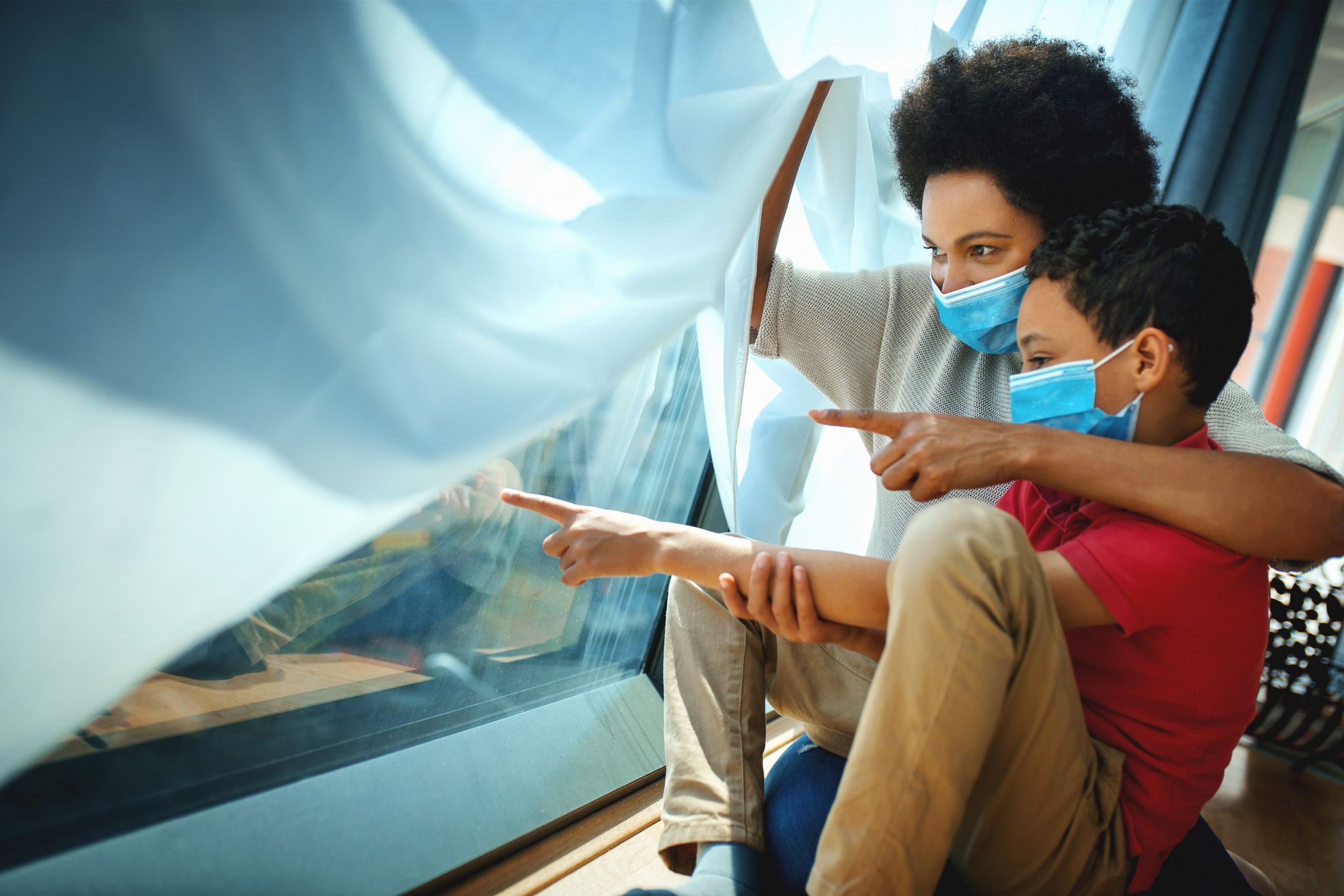 Mother and son in pandemic quarantine looking though window.