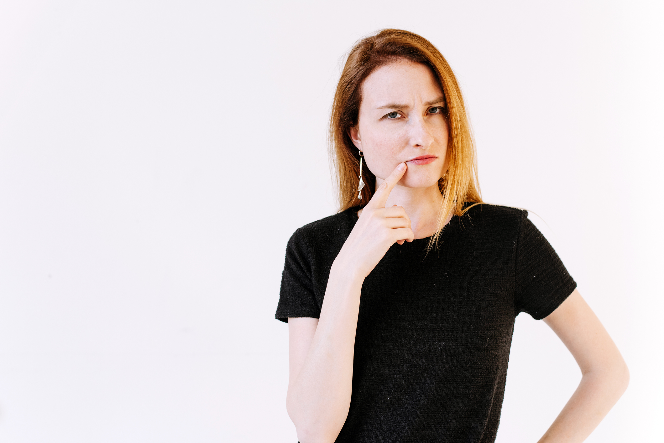 The thinking girl is on the white background. The girl with a finger at the mouth