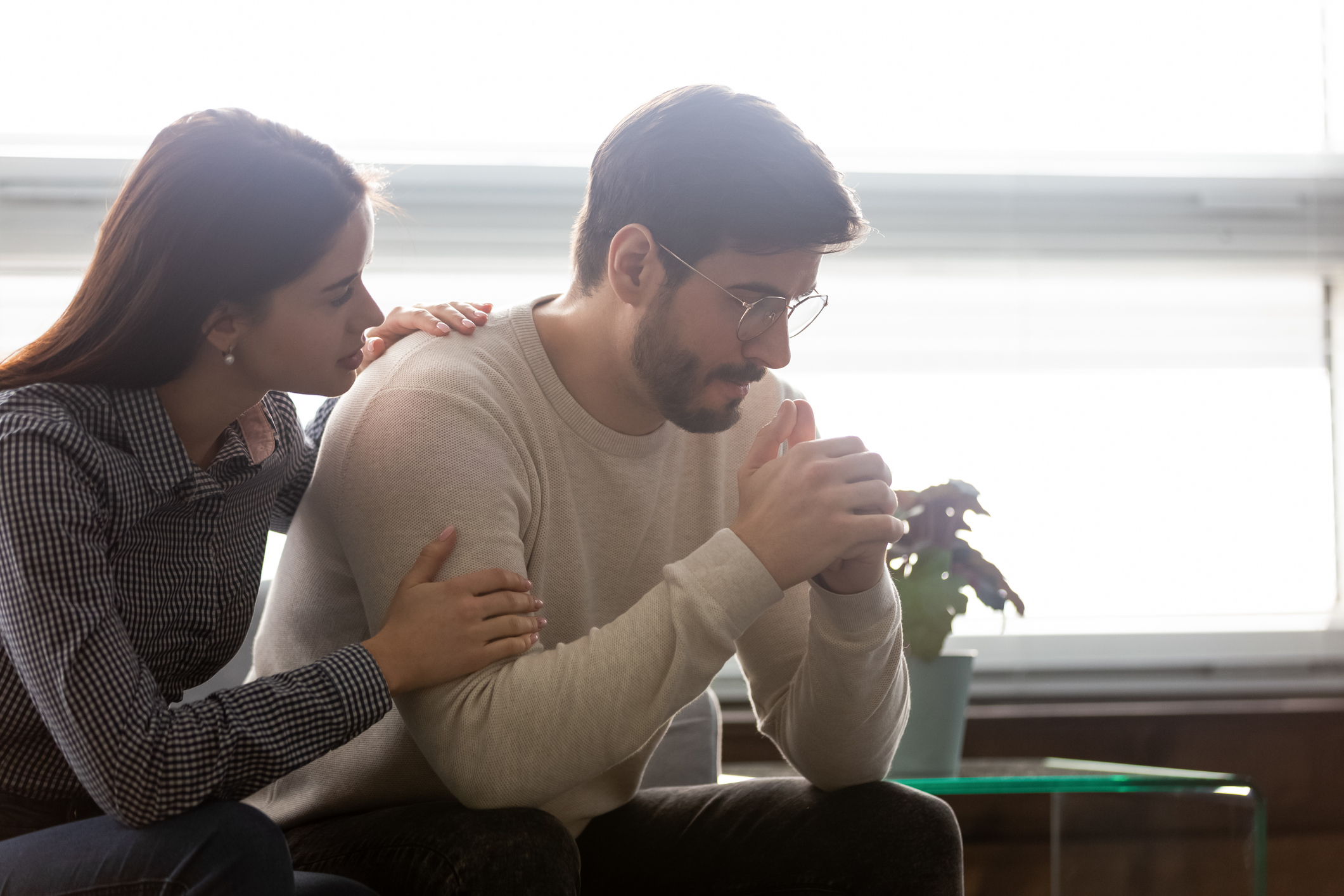 Couple sit on sofa caring wife hugs disappointed sad frustrated husband