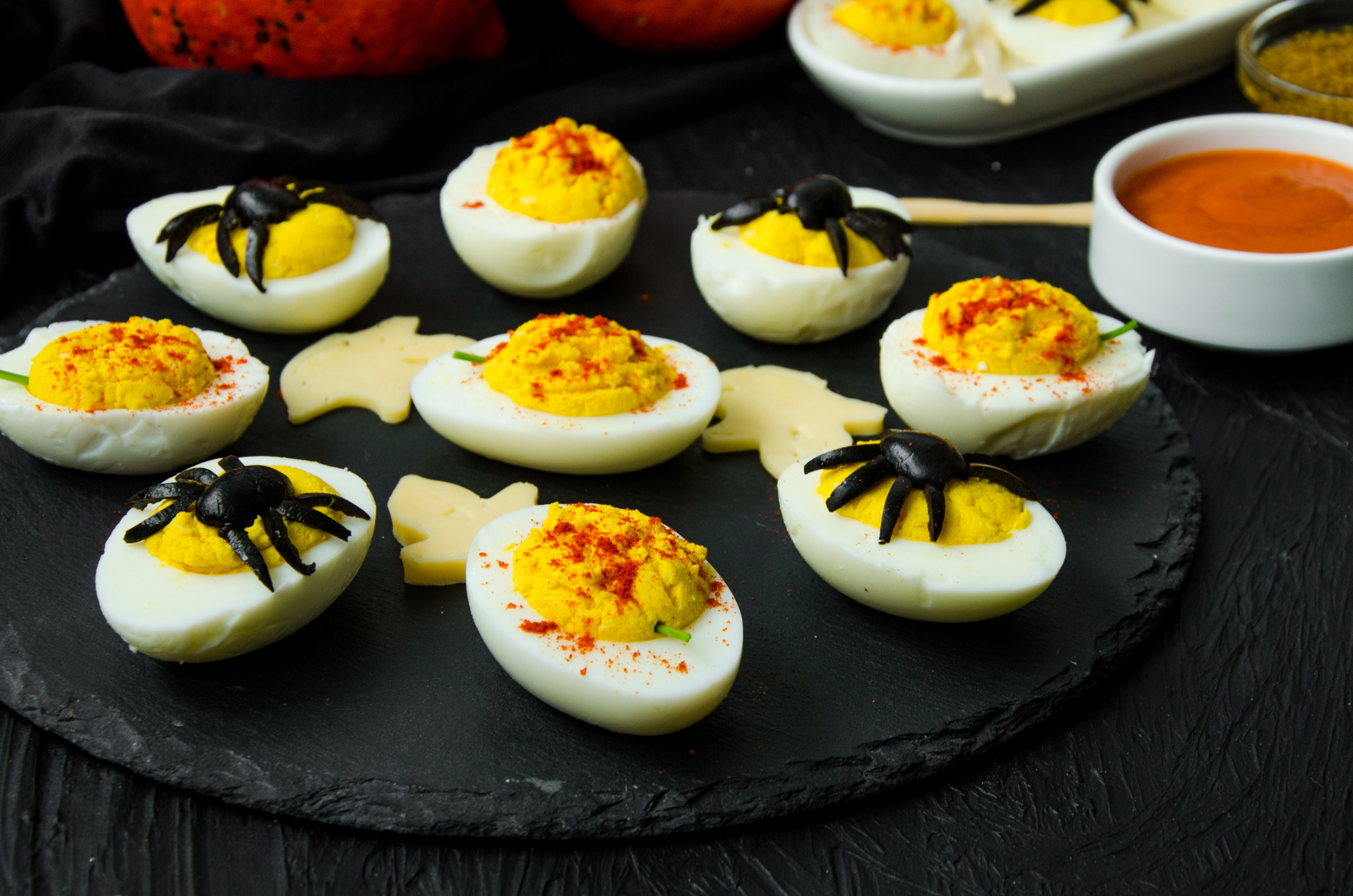 Halloween stuffed eggs with cheese and mustard on a black stone. Pumpkin Eggs with smoked paprika, Spider Eggs with olives. Fun food idea for halloween party.