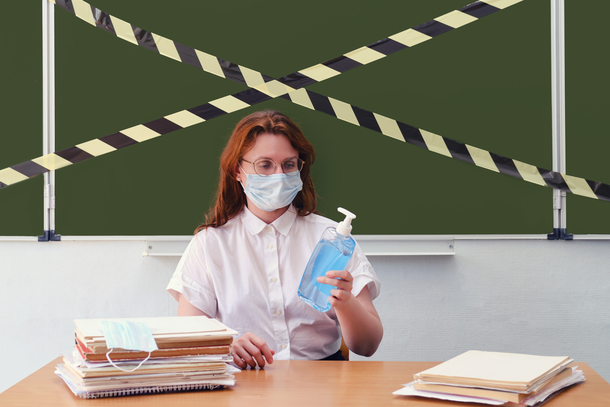 A teacher in a medical mask looks at an antiseptic to disinfect the school classroom. A sanitizer is held by a woman to wash her hands during the flu virus epidemic