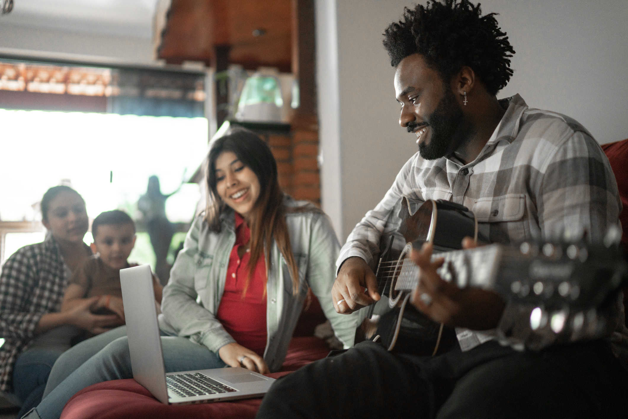 Young man playing acoustic guitar in front of a laptop at home