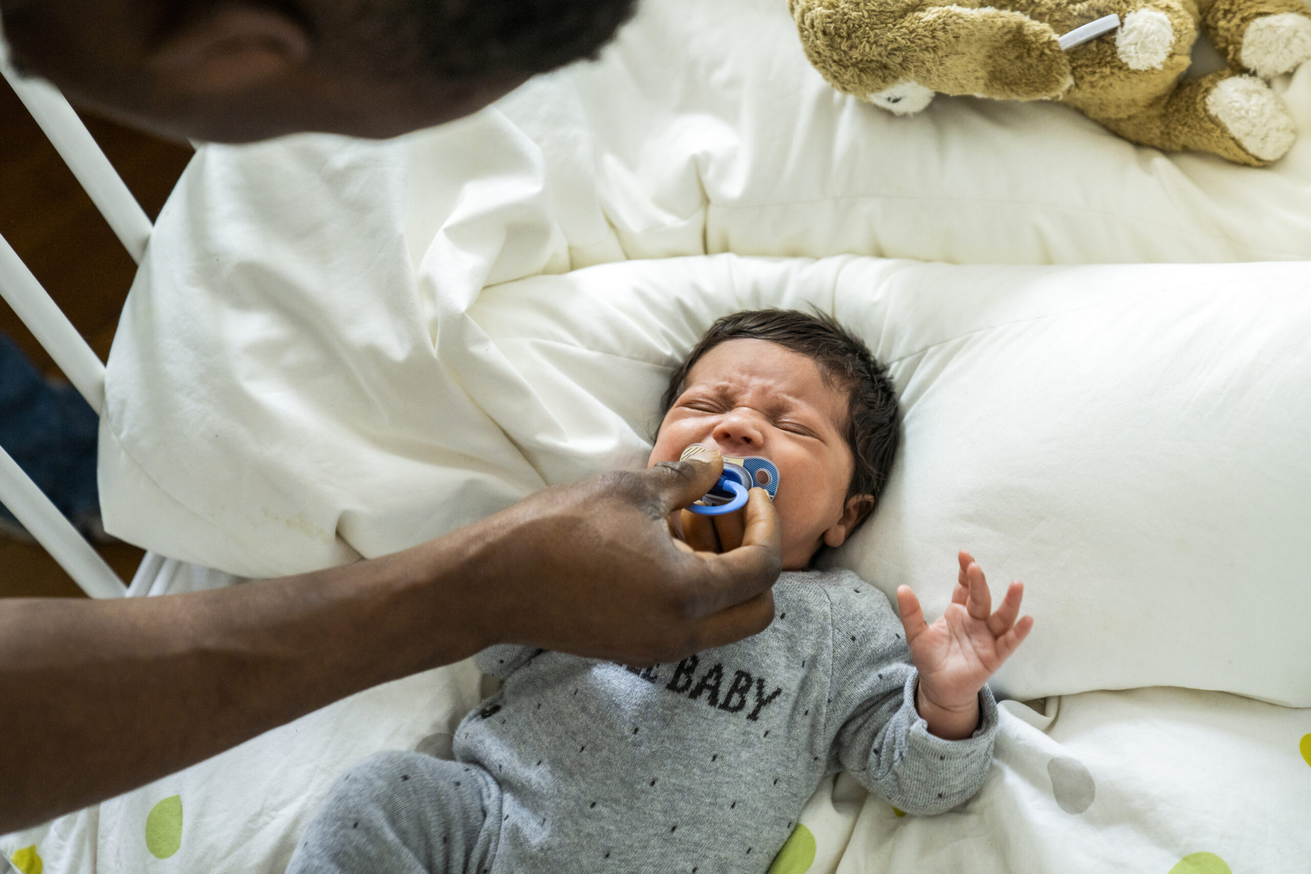 Father giving pacifier to crying baby in crib