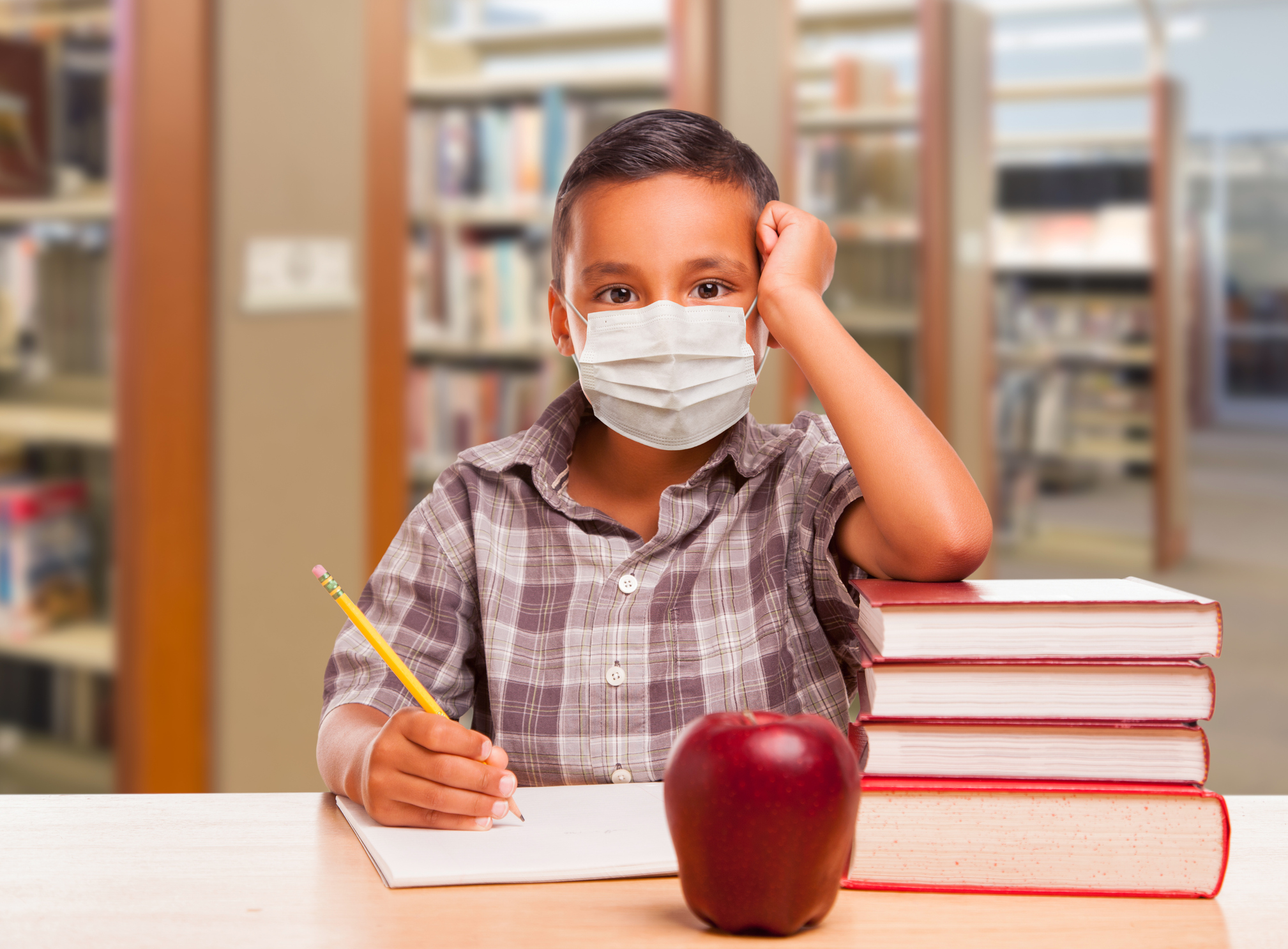 Hispanic Boy Wearing Face mask with Books, Apple, Pencil and Paper at Library