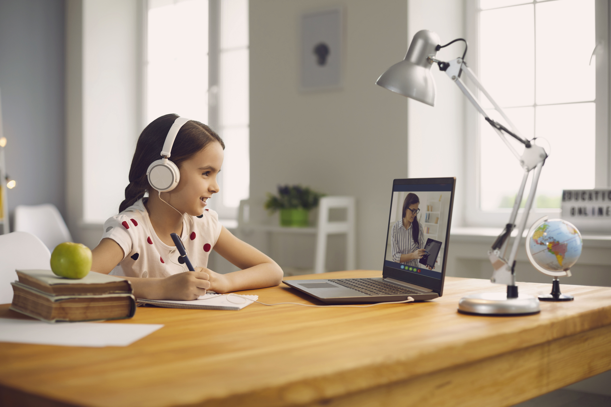 Online student education. Schoolgirl listens to a lecture of a teacher using a laptop video call lesson sitting at a table at home.