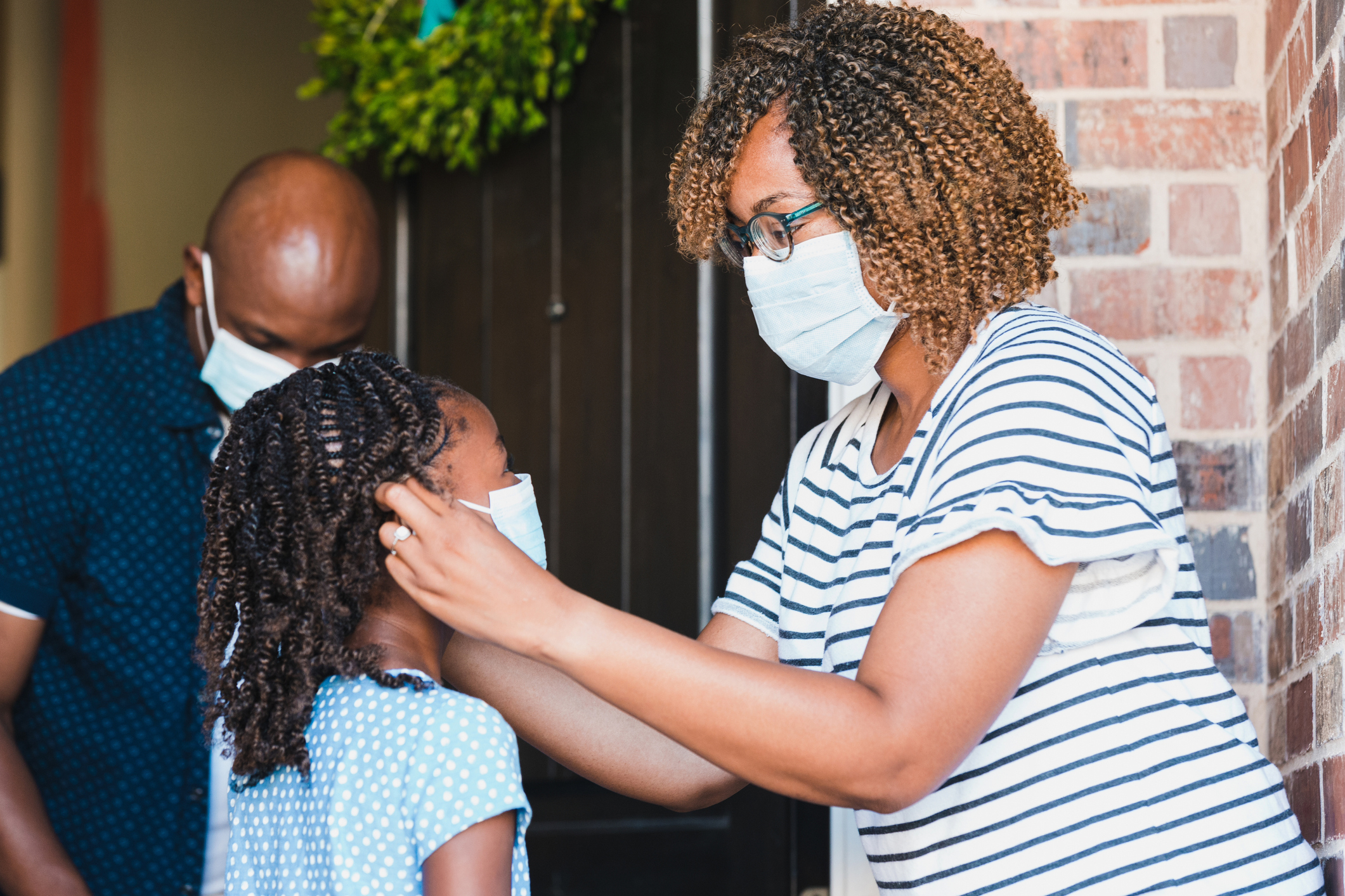 Mom helps daughter put on  protective face mask