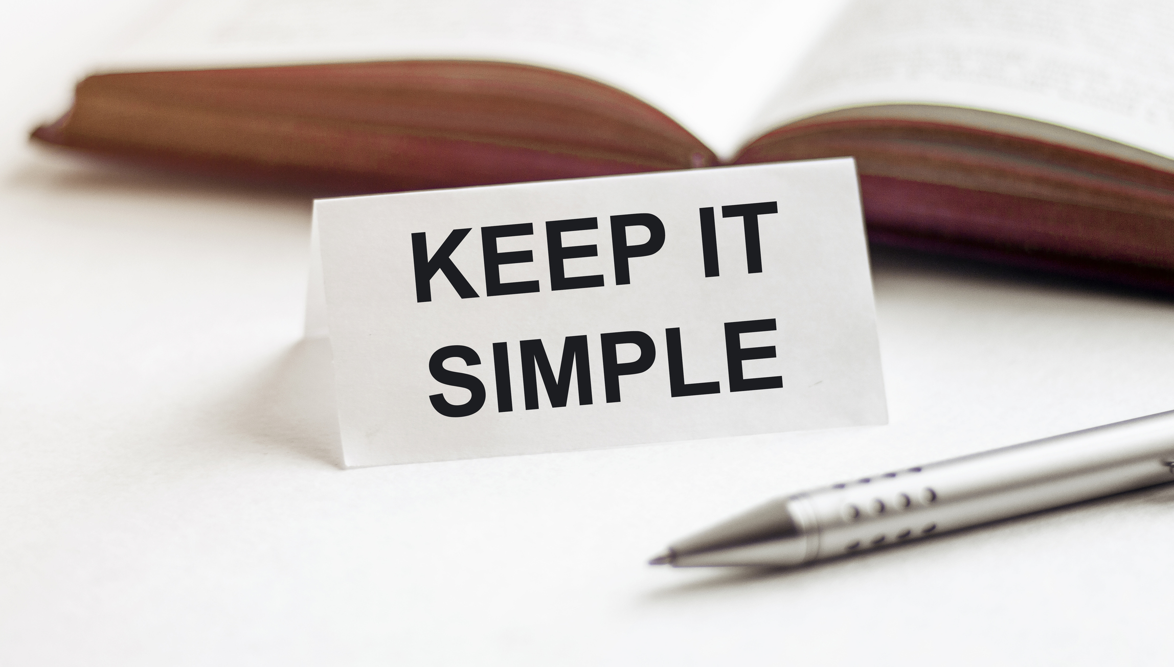 piece of paper with text Keep It Simple on the background of books, pens, on a white background