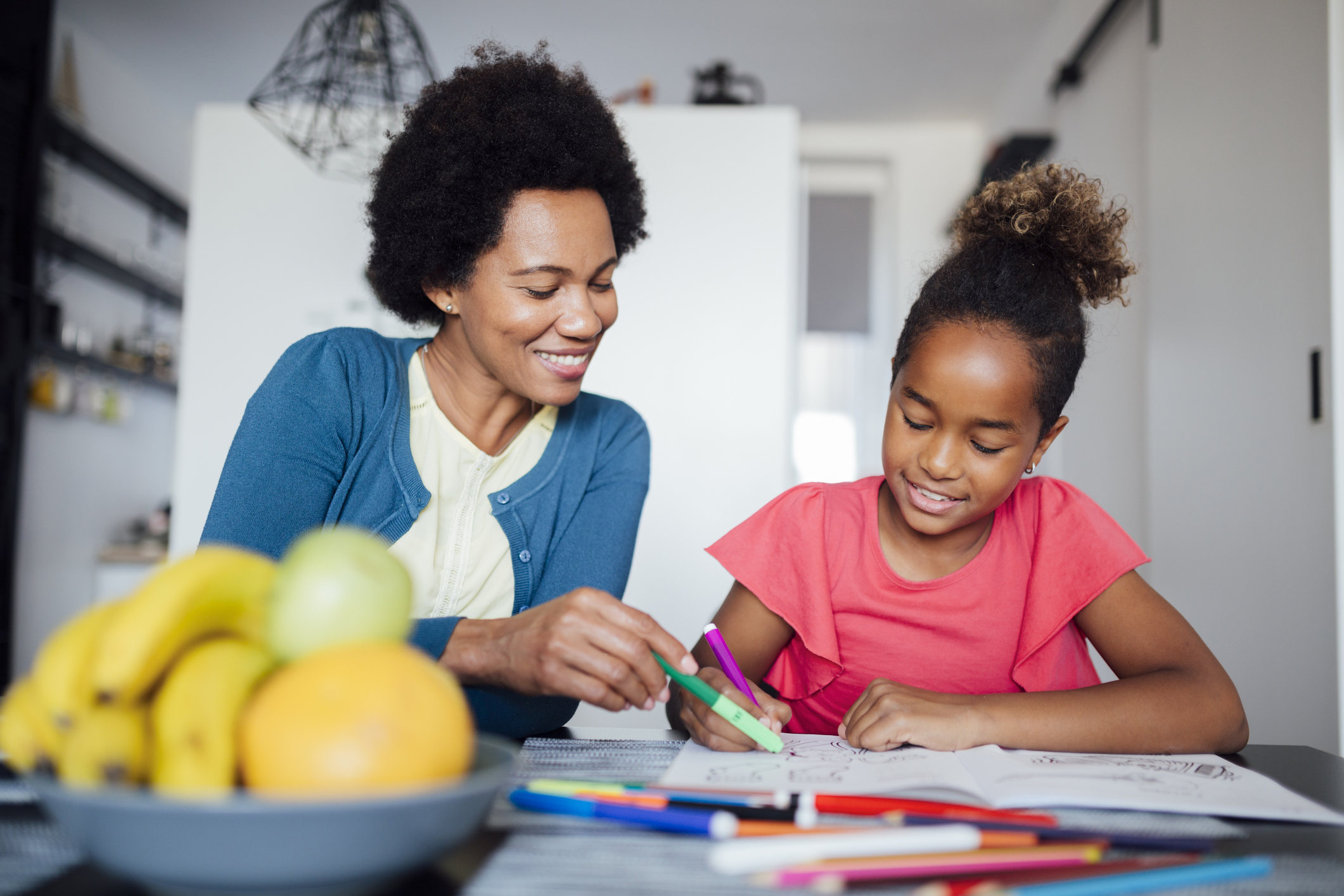 Happy African American mother tutoring her daughter at home