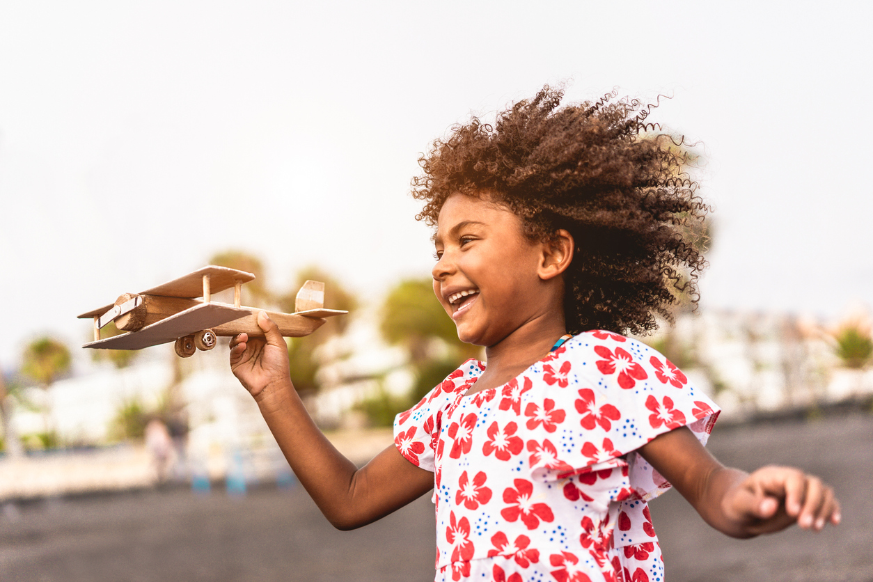 African kid running on the beach while playing with wood toy airplane at sunset, Travel and youth lifestyle concept - Main focus on hand holding plane