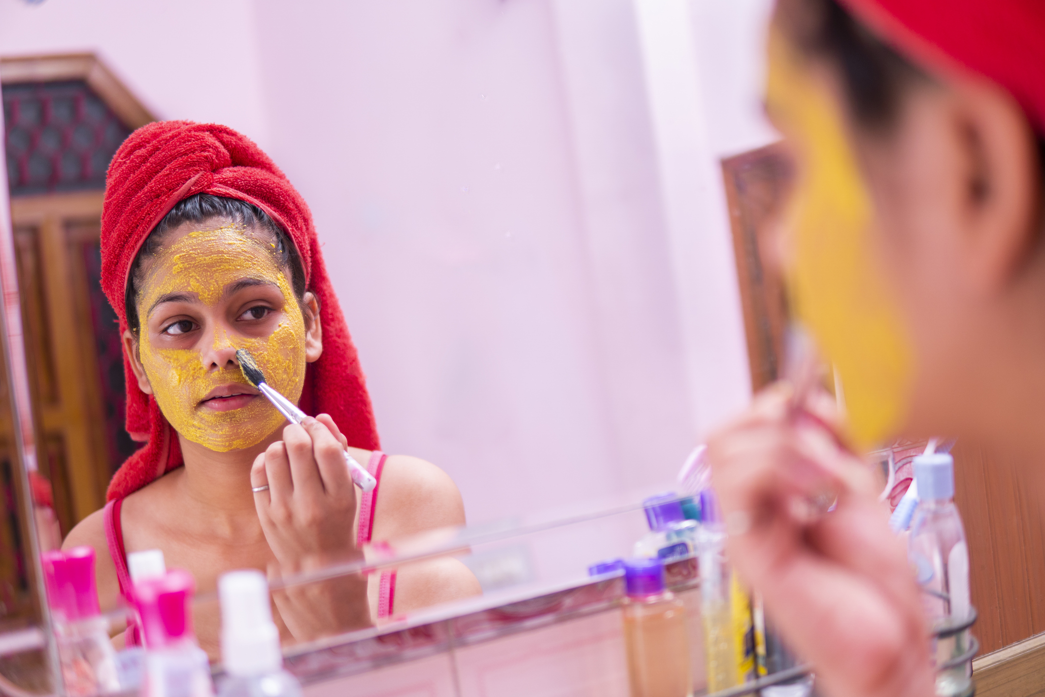 Beautiful girl applying yellow turmeric face pack on face.