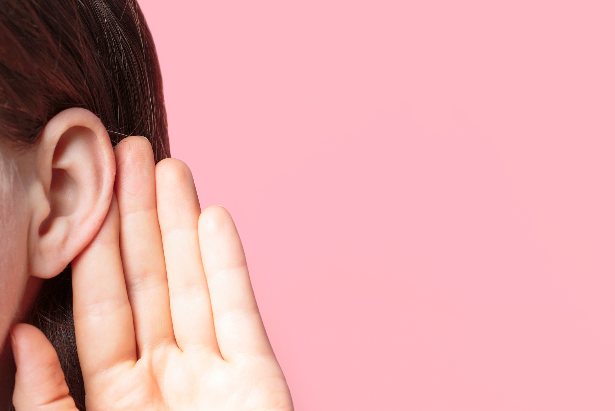 The girl listens attentively with her palm to her ear close-up on pink background