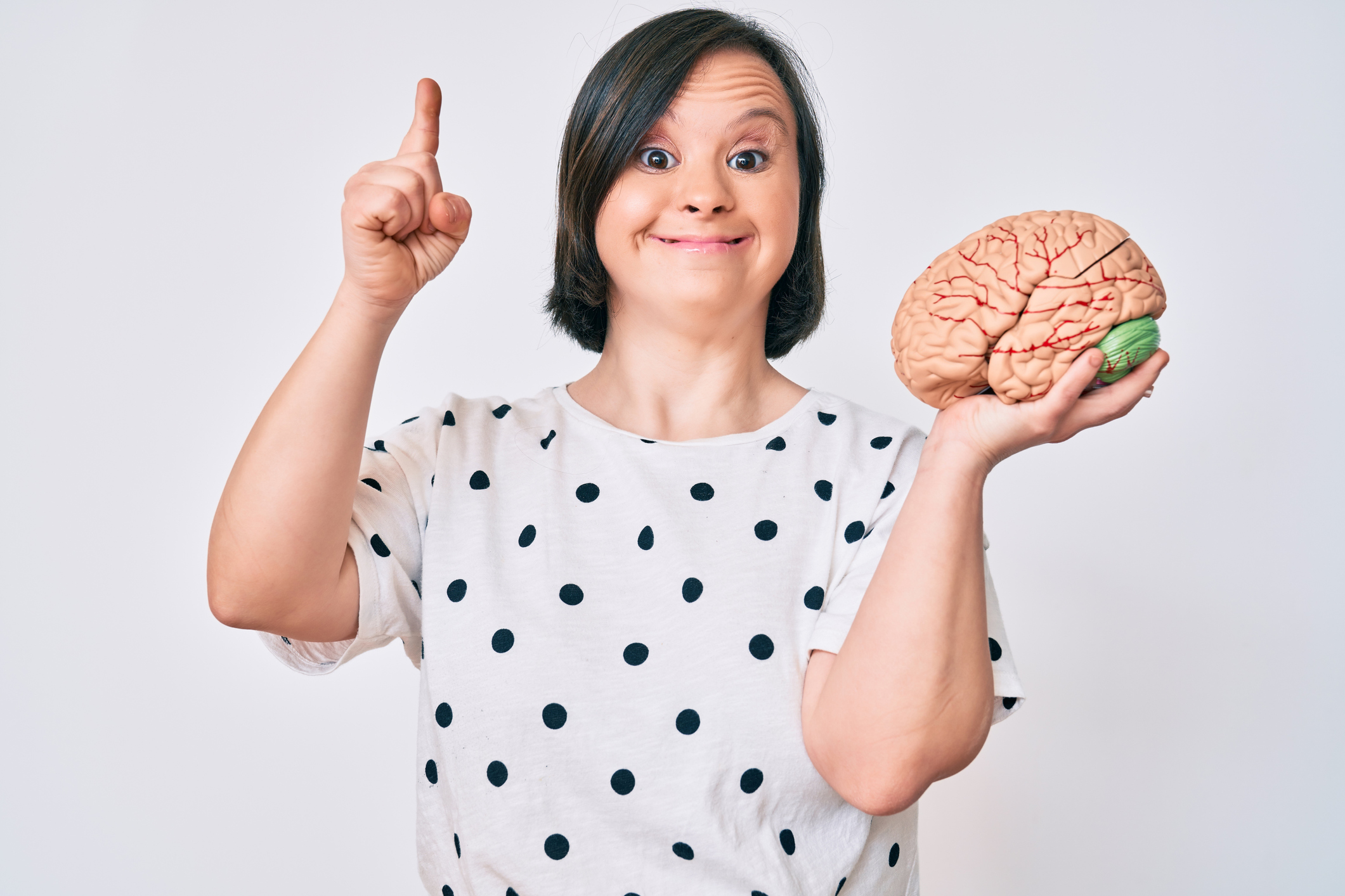 Brunette woman with down syndrome holding brain smiling with an idea or question pointing finger with happy face, number one