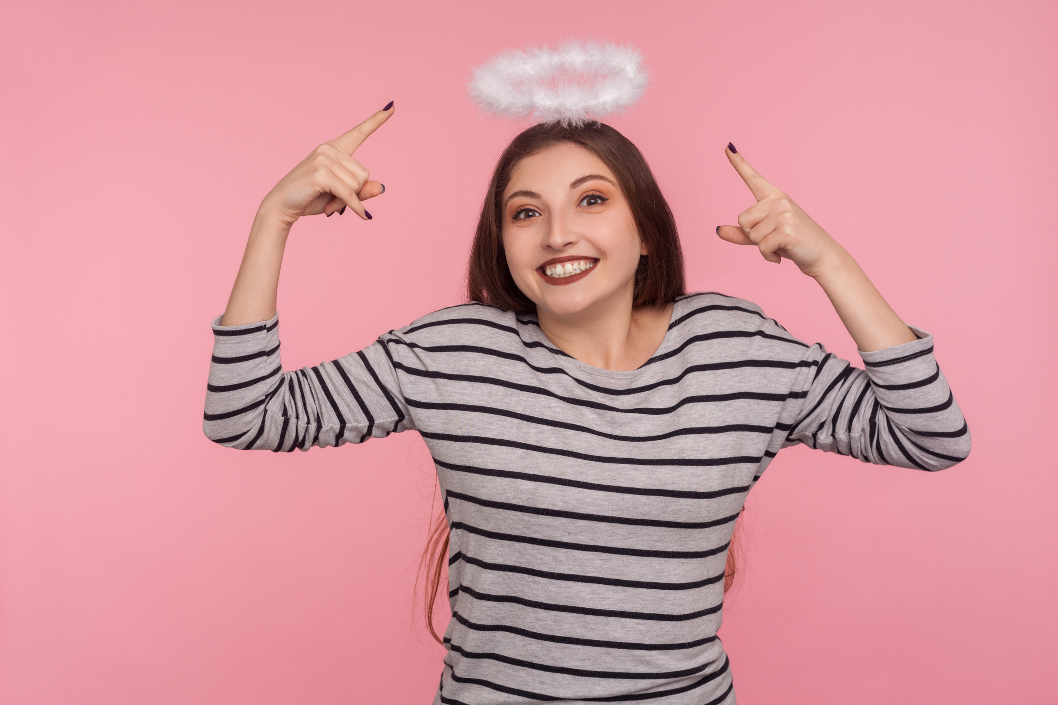 Look, I'm saint angel! Portrait of lovely joyful woman pointing at holy nimbus over head, showing aureole