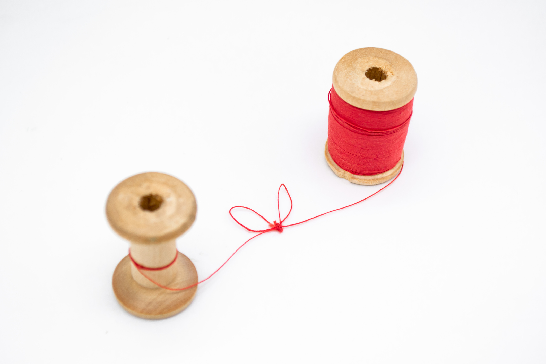 Two wooden spools of thread. One is full, the other almost empty, connected by a single thread with a knot in the shape of a heart. Love and togetherness as a concept, without people