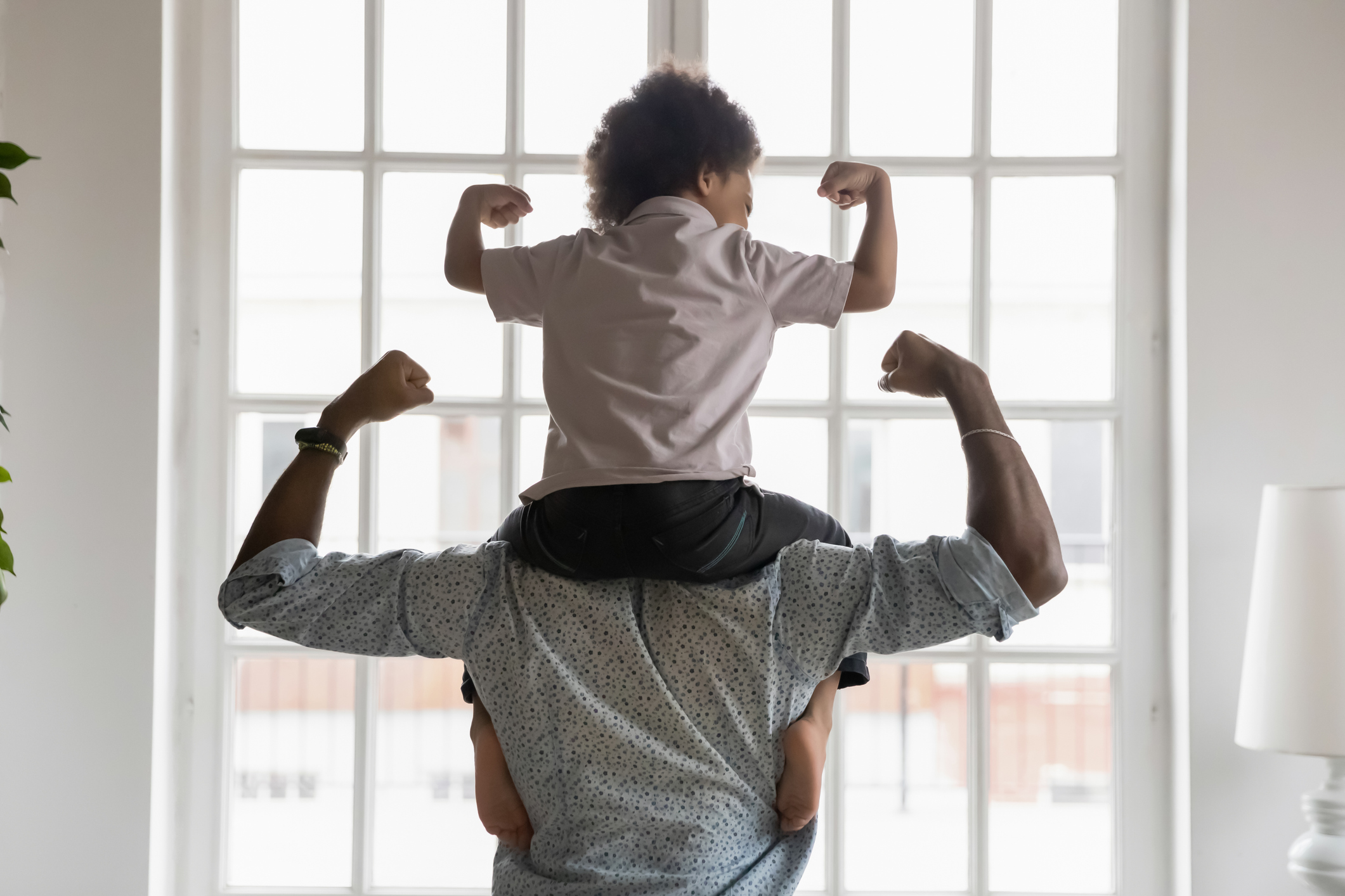 African american father with little son on shoulders showing biceps.