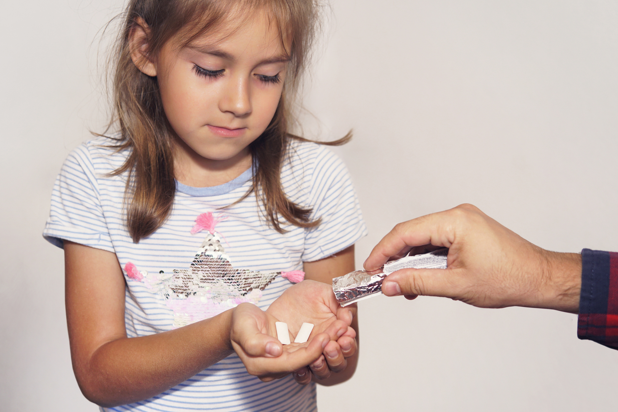 man gives mint chewing gum to a child. Cleaning your teeth with chewing gum after eating. Fresh breath. girl takes stick of gum. bad habit, harmful habit, pernicious habit, unhealthy habit