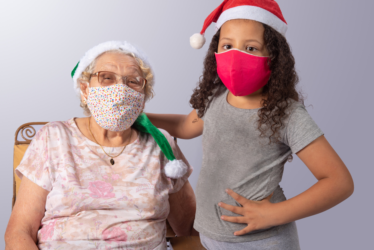 Elderly woman and child with Christmas hat and mask holding white sign, gray gradient background, selective focus.