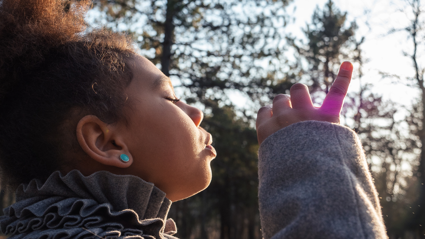 Wonderful childhood. Happy Afro-American girl playing in the park, making soap bubbles and laughing.